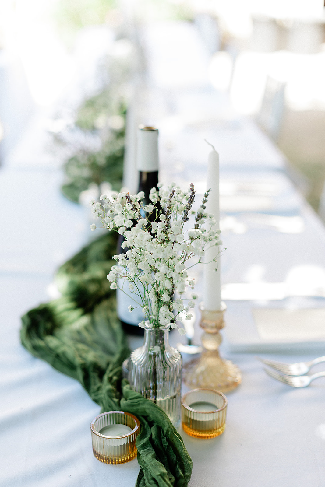 Elegant table centerpiece with white flowers, brass candles, and green runner at wedding reception