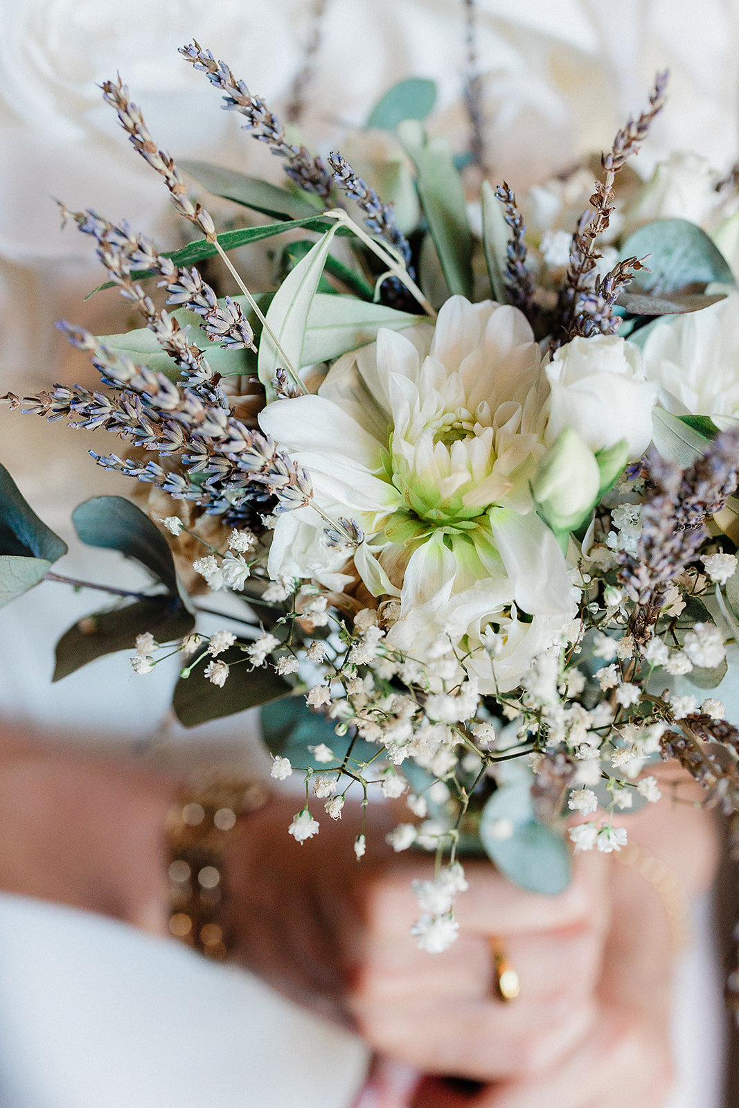 Close-up bridal bouquet with white dahlias, lavender, and eucalyptus at garden wedding