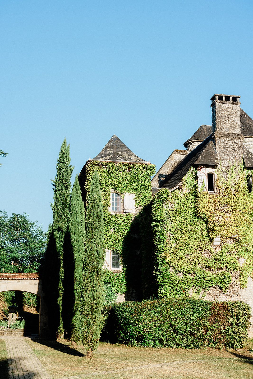 Historic stone château with ivy-covered walls and formal gardens with topiary and cypress trees