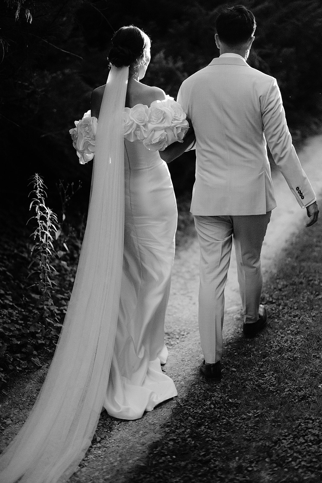 Bride and groom walking together down garden path in black and white portrait