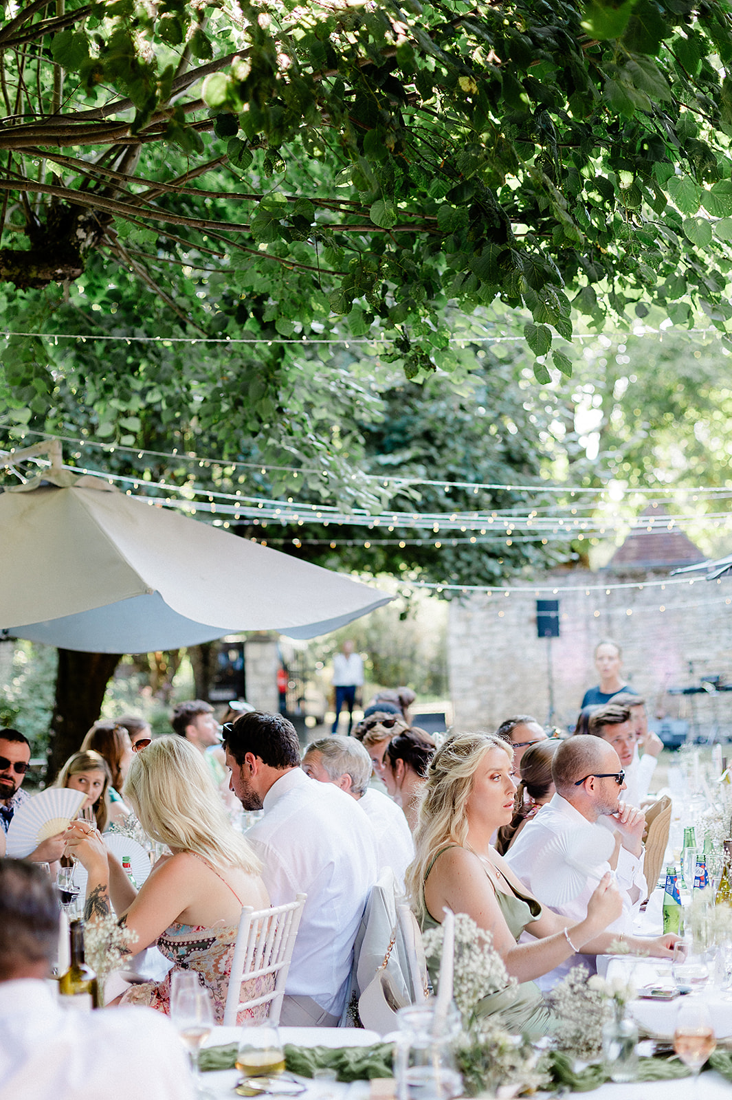 Wedding reception dinner with guests dining at long tables in outdoor garden courtyard with string lights