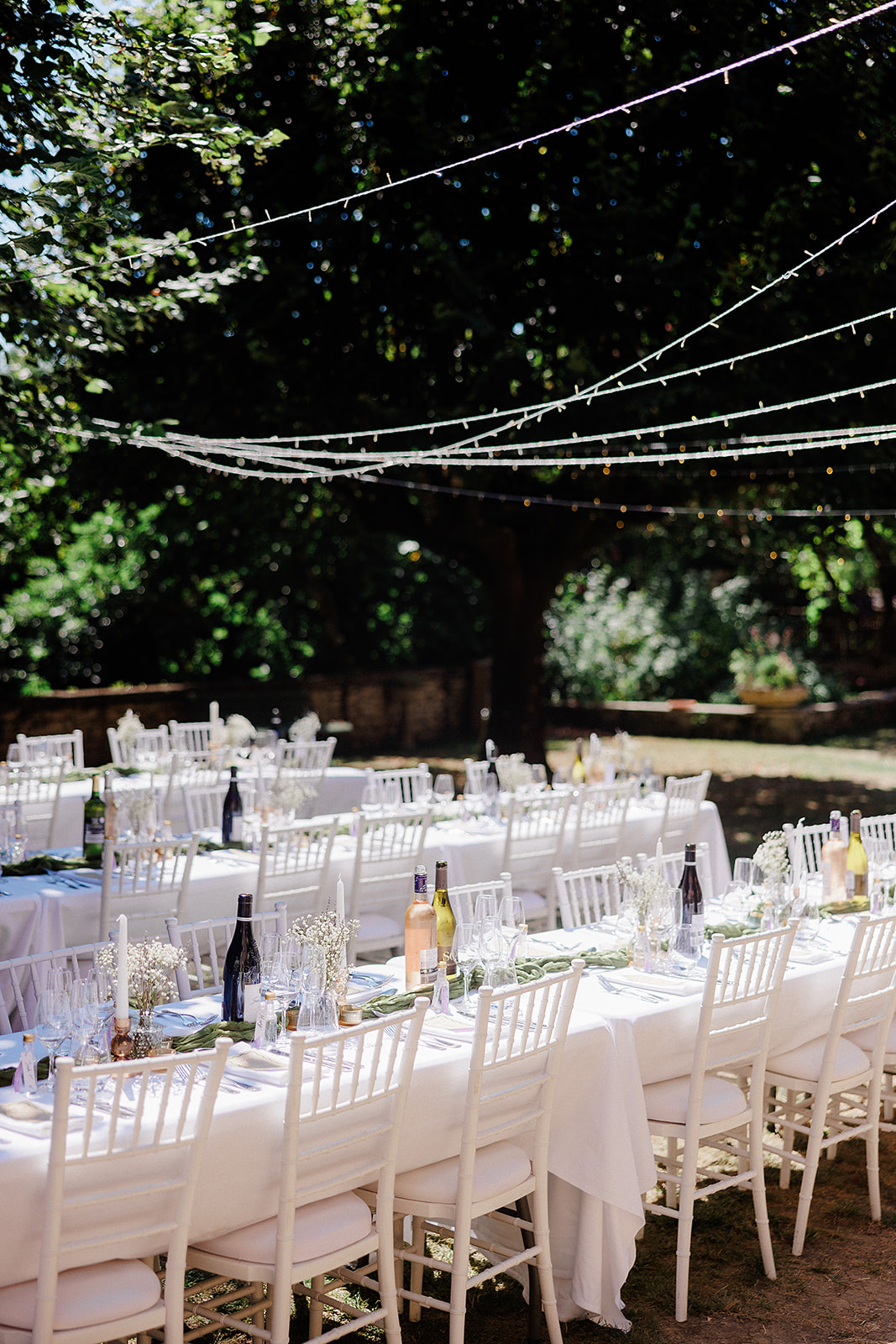 Outdoor reception tables with ivory linens and bistro lighting in garden courtyard