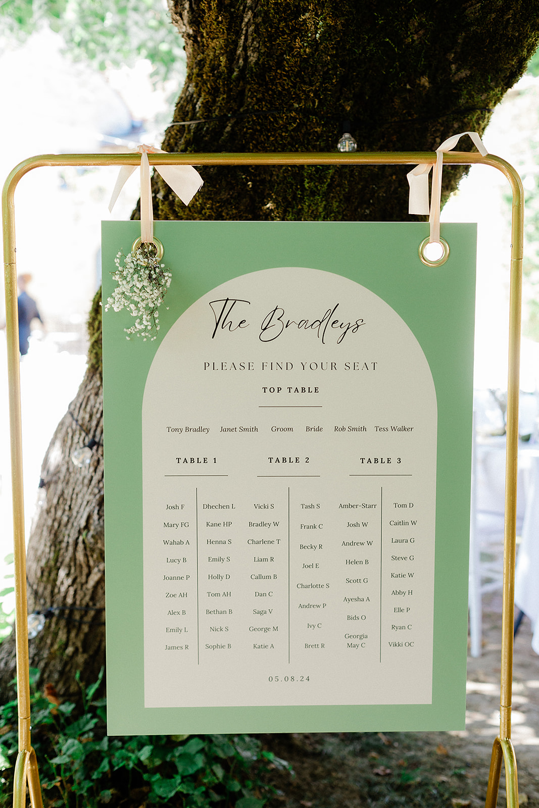 Sage green seating chart with brass easel at outdoor garden wedding reception