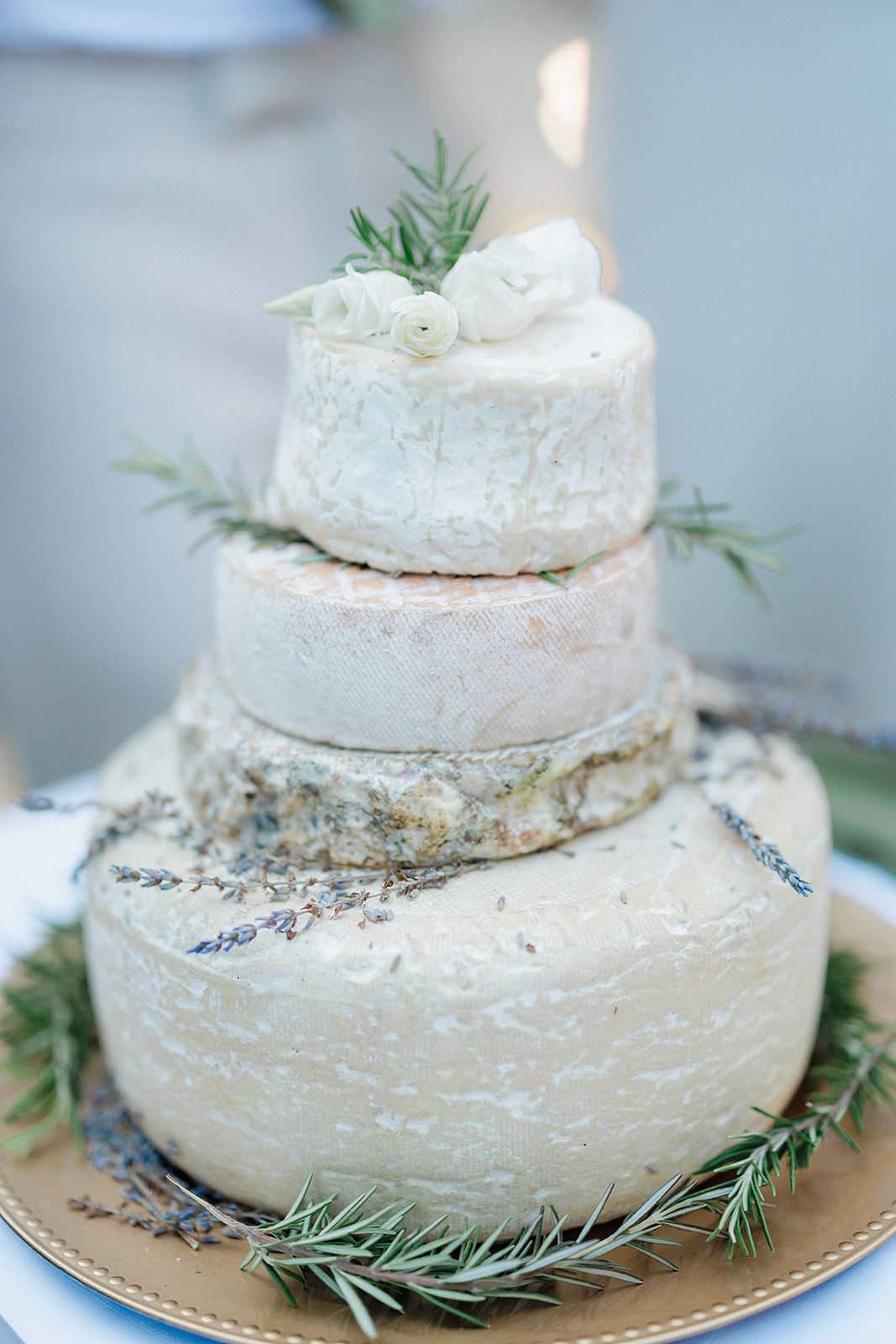 Four-tiered rustic wedding cake with herbs and ranunculus flowers at outdoor venue