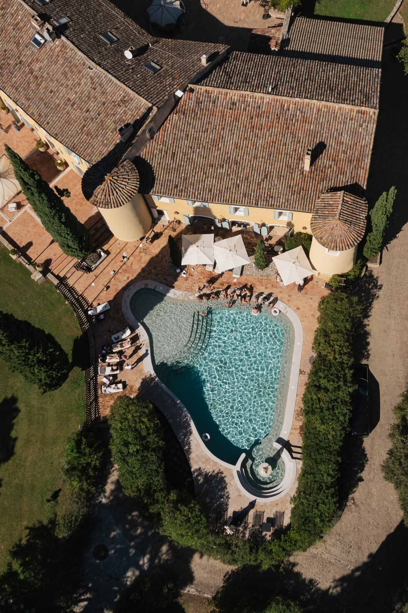 Aerial view of poolside wedding reception at Tuscan villa with cypress trees and terracotta roofing
