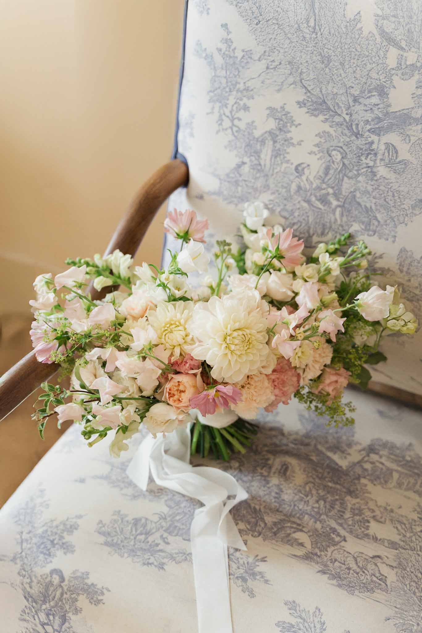 Bridal bouquet with ivory dahlias and blush roses against blue toile dress at wedding venue