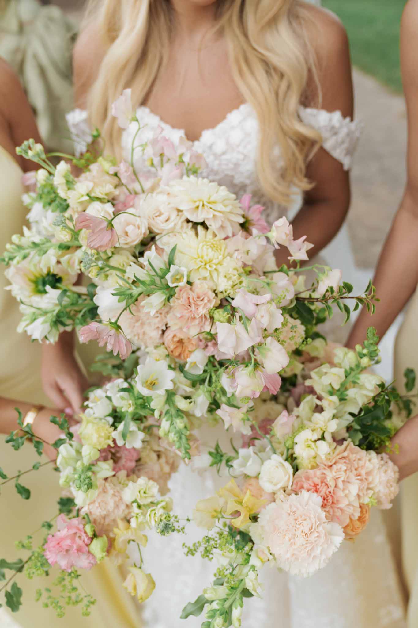 Bride holding cascading garden bouquet with blush dahlias and roses at outdoor wedding venue