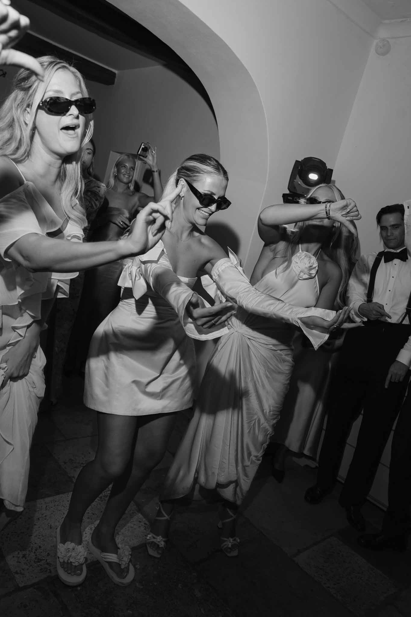 Bride dancing with guests in sunglasses at modern indoor wedding reception