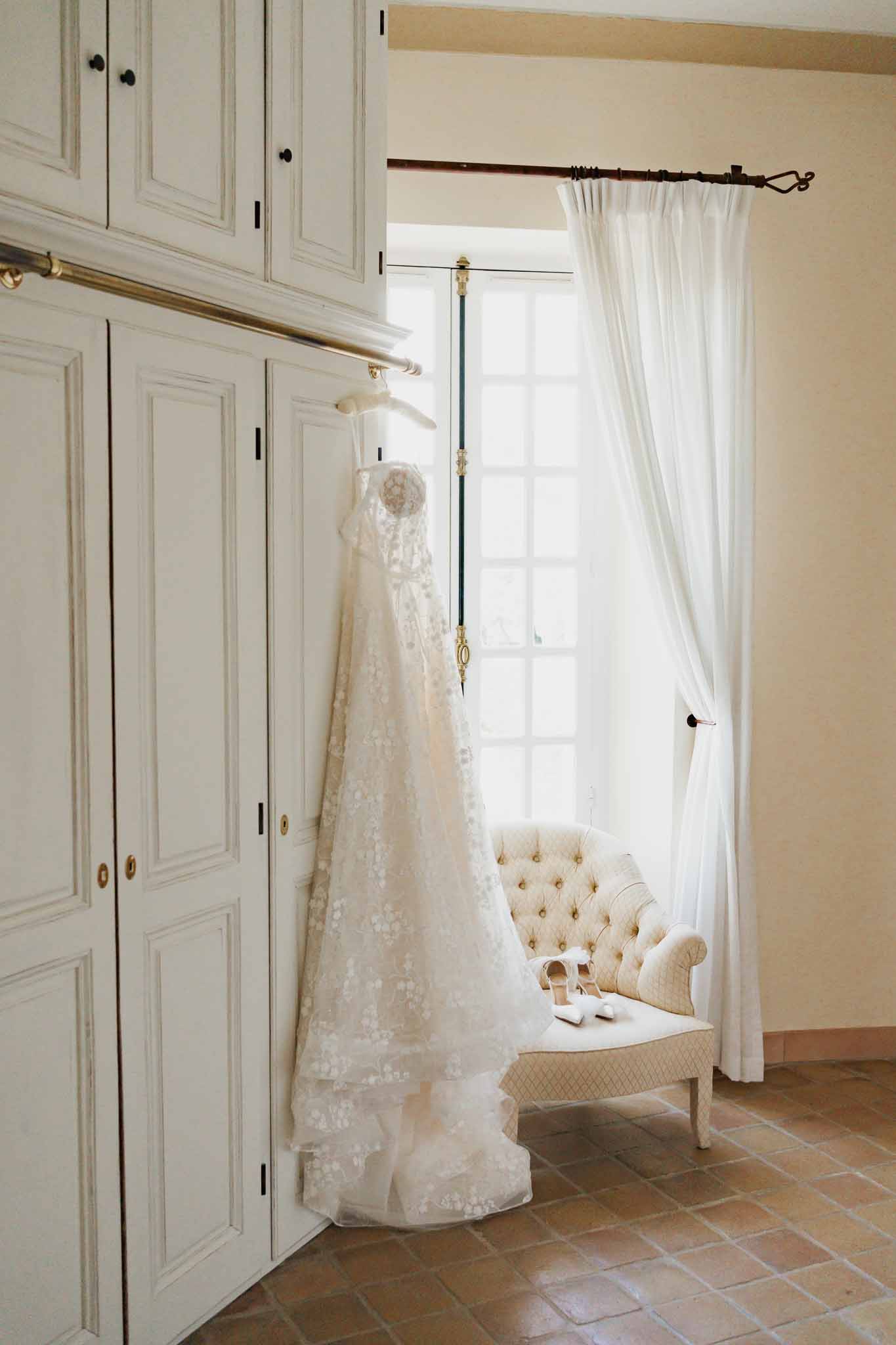 Ivory lace wedding dress hanging in bridal suite dressing room with cream decor