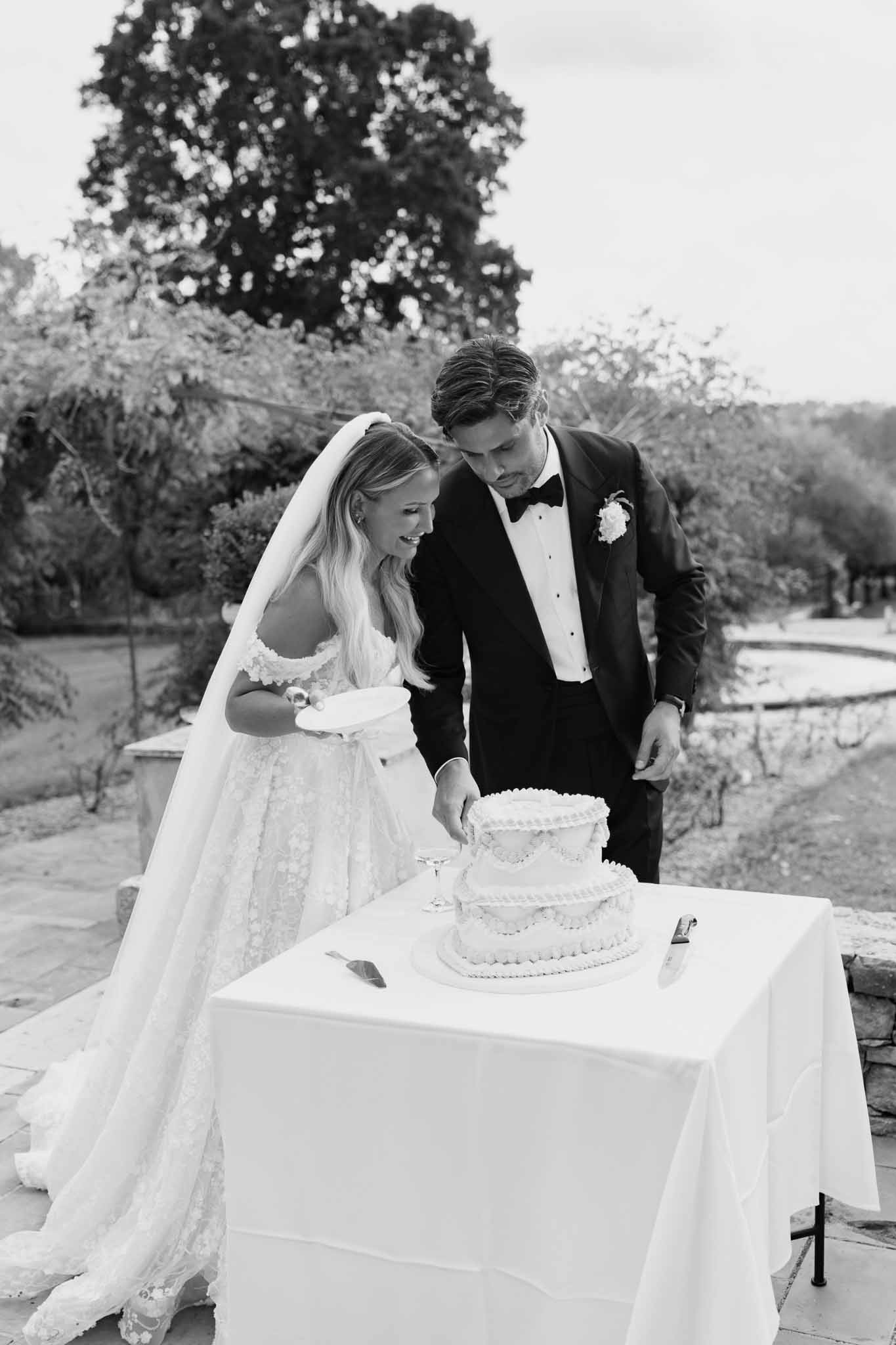 Bride and groom cutting wedding cake during outdoor reception at garden estate