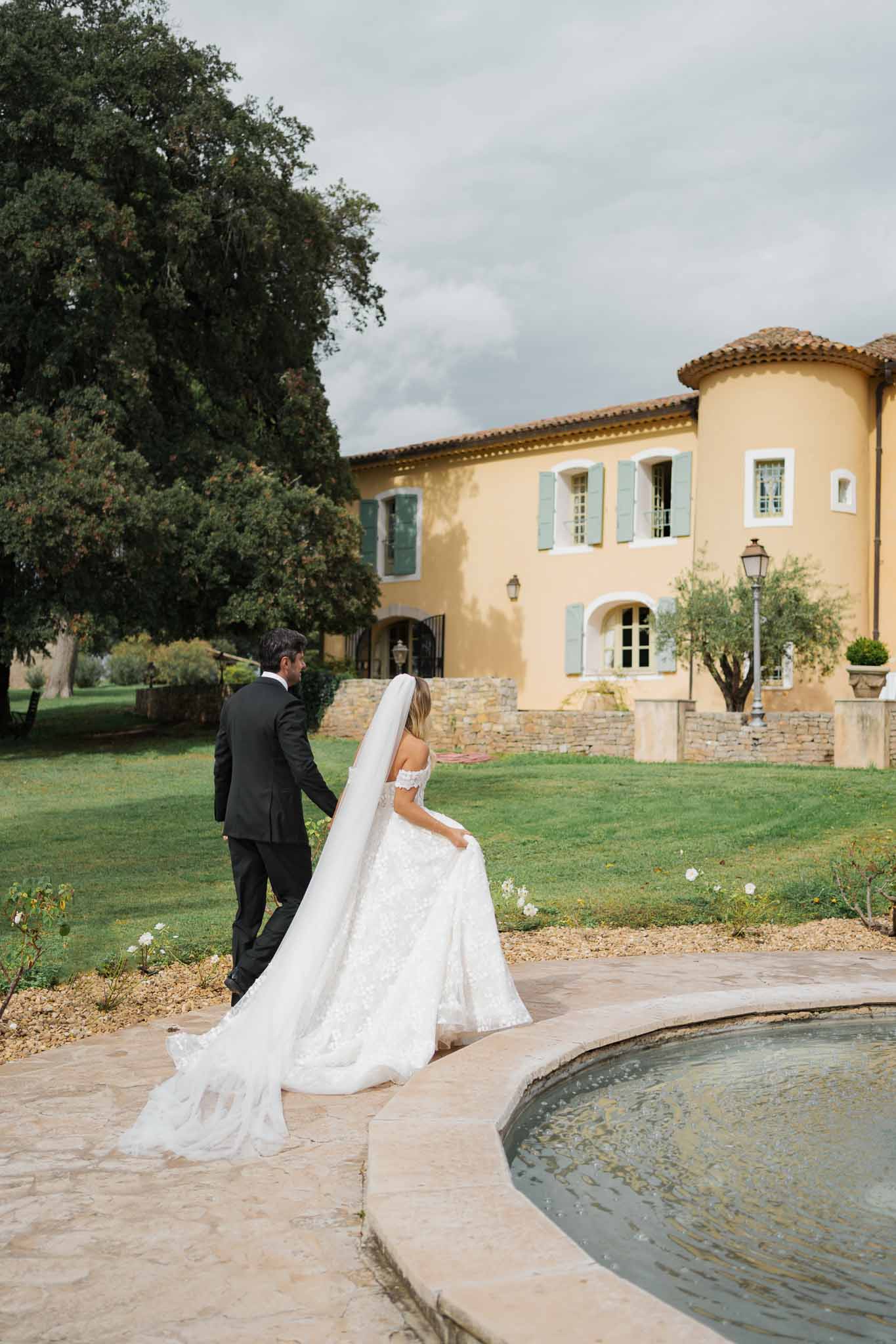 Bride and groom walking together on terracotta pathway at Tuscan-style villa with pool and gardens