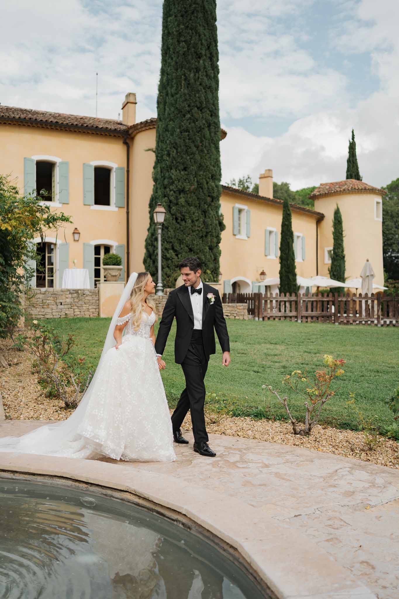 Bride and groom walking beside pool at Tuscan villa during outdoor wedding reception
