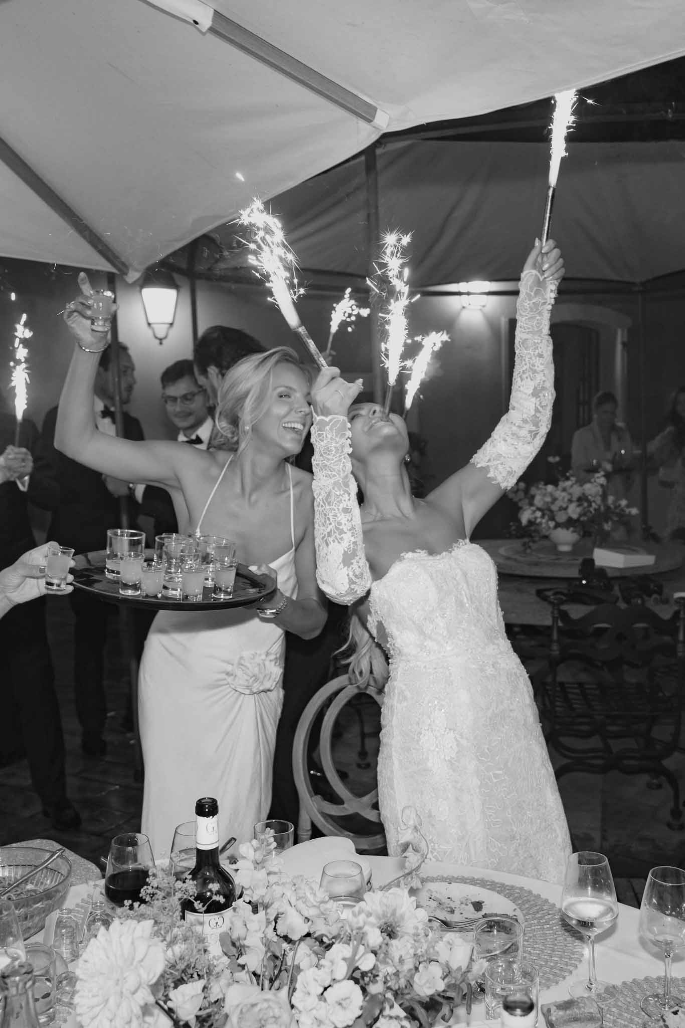 Bride and guest holding sparklers at marquee tent reception with white floral table setting