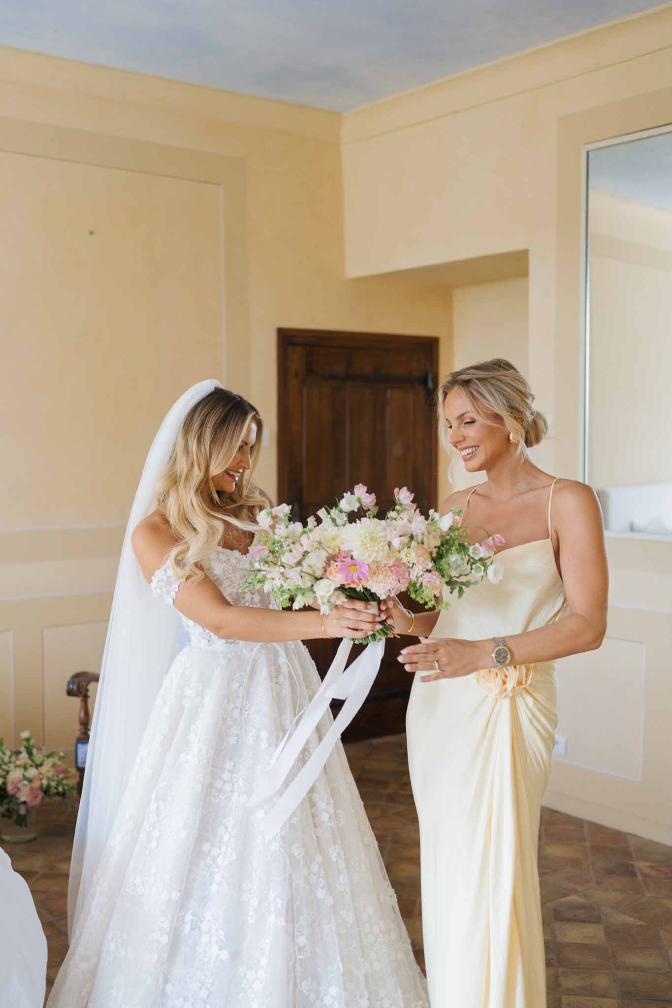 Bride and bridesmaid admiring bridal bouquet during getting ready moment in elegant interior room