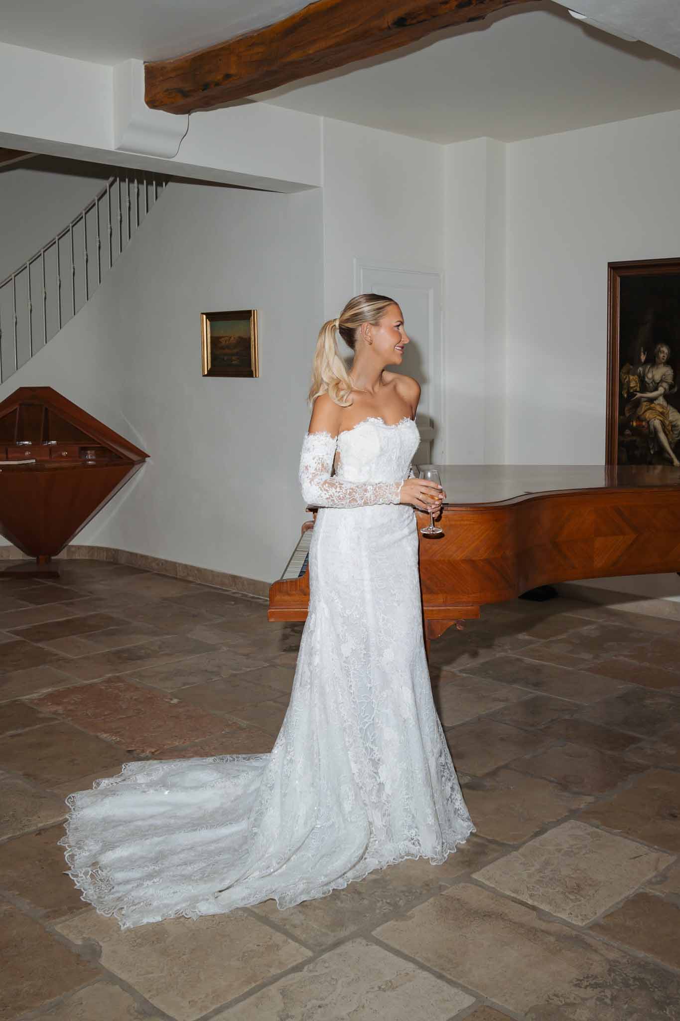 Bride in ivory lace wedding dress with champagne flute in modern architectural venue interior