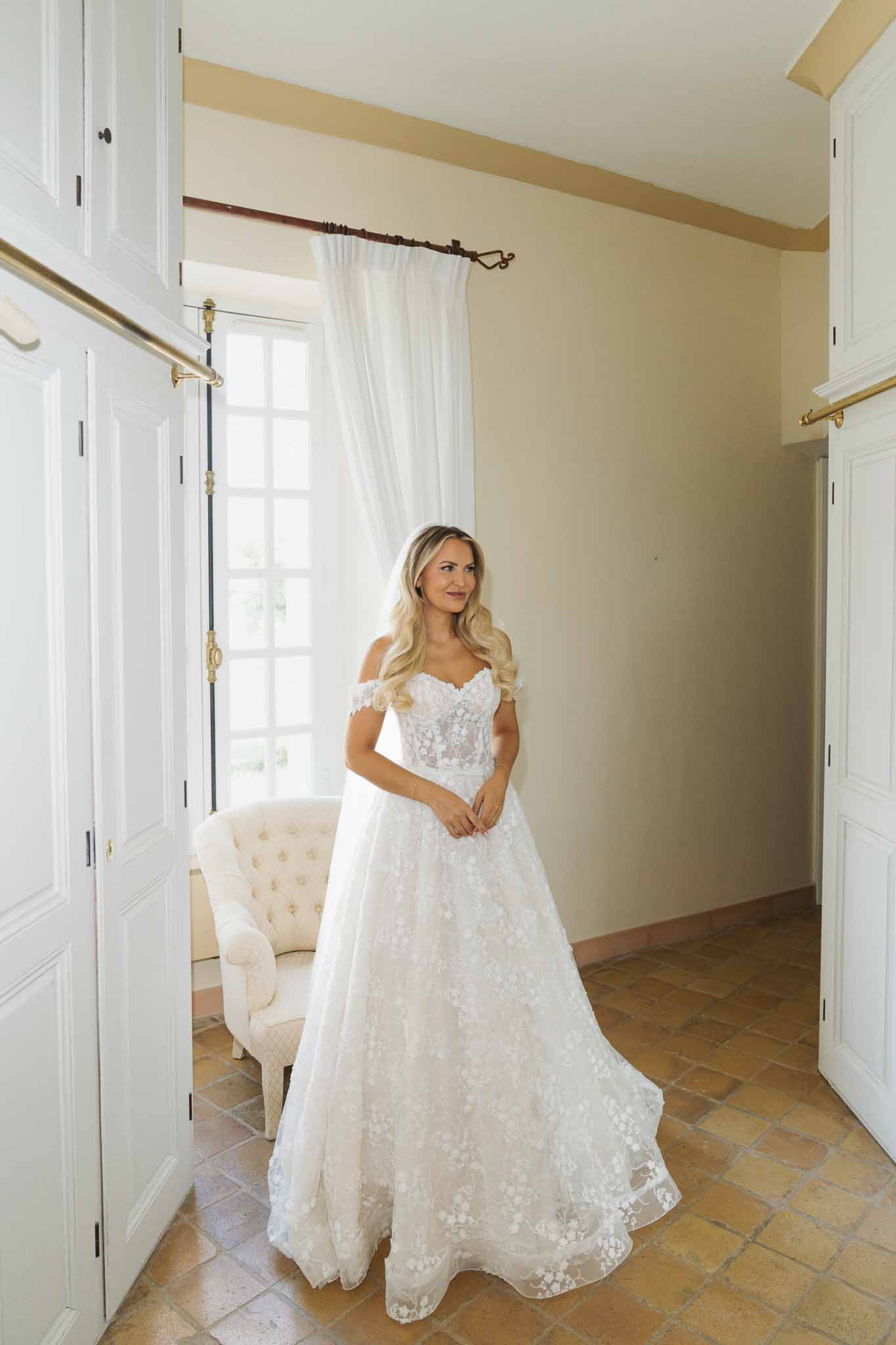 Bride in ivory lace wedding dress posing in elegant dressing room during getting ready preparations