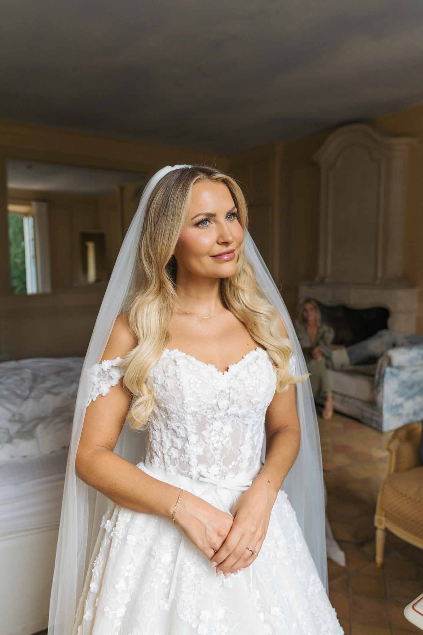 Bride in white lace wedding dress and ivory veil posing in indoor dressing room
