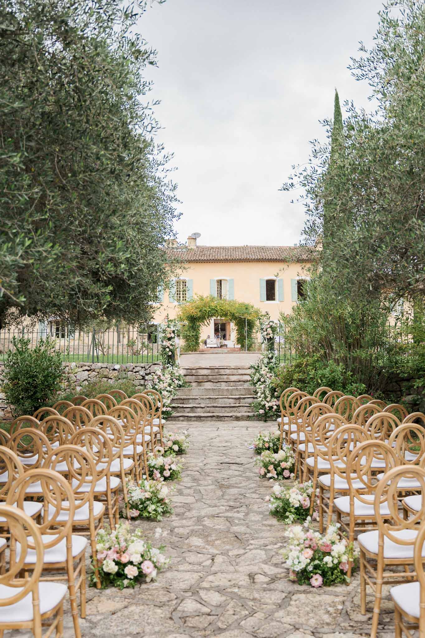 Wedding ceremony setup in courtyard garden at Provençal villa with stone aisle and bentwood chairs