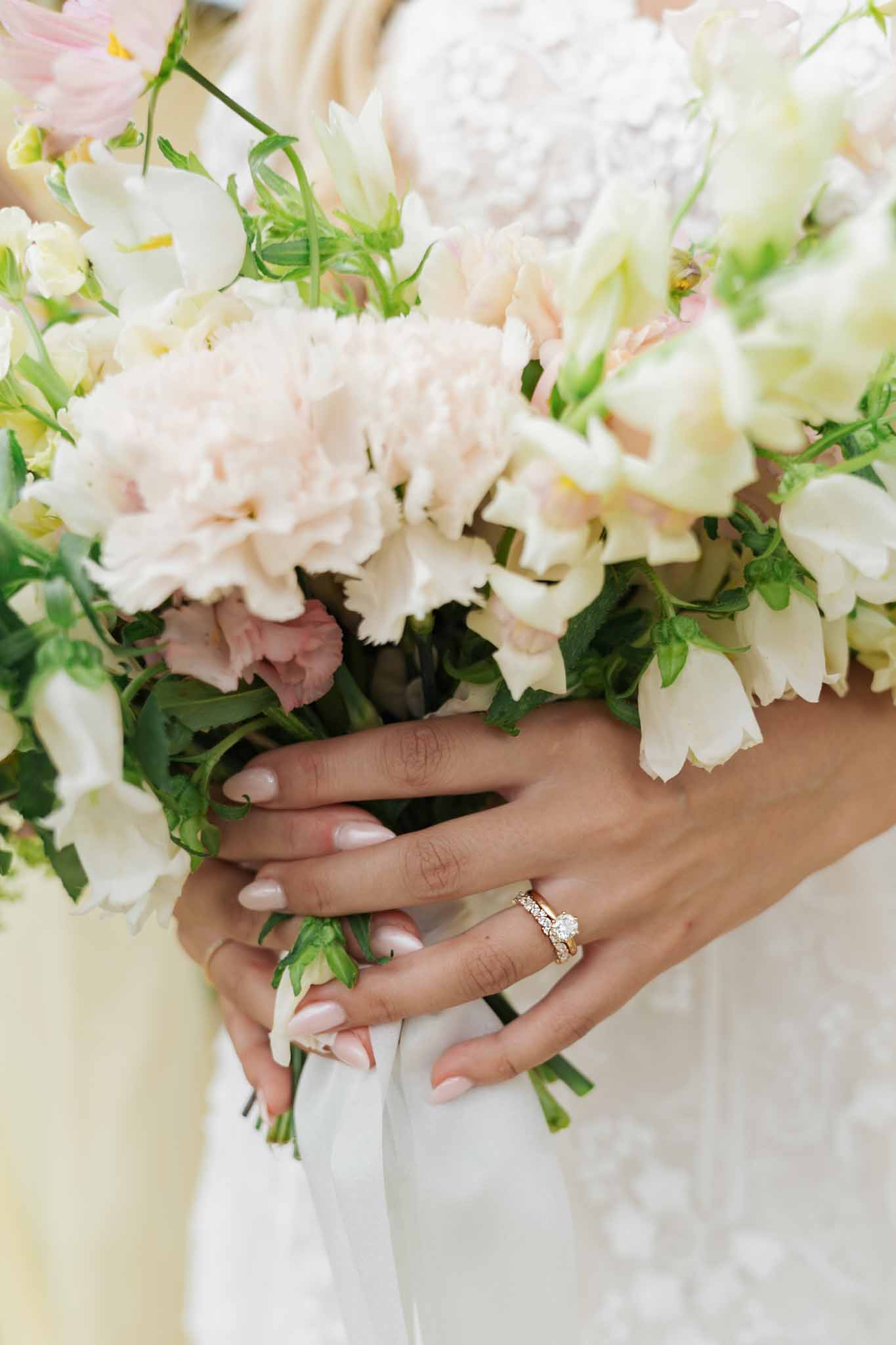 Bride's hands holding ivory and blush peony bouquet showing engagement ring and wedding band