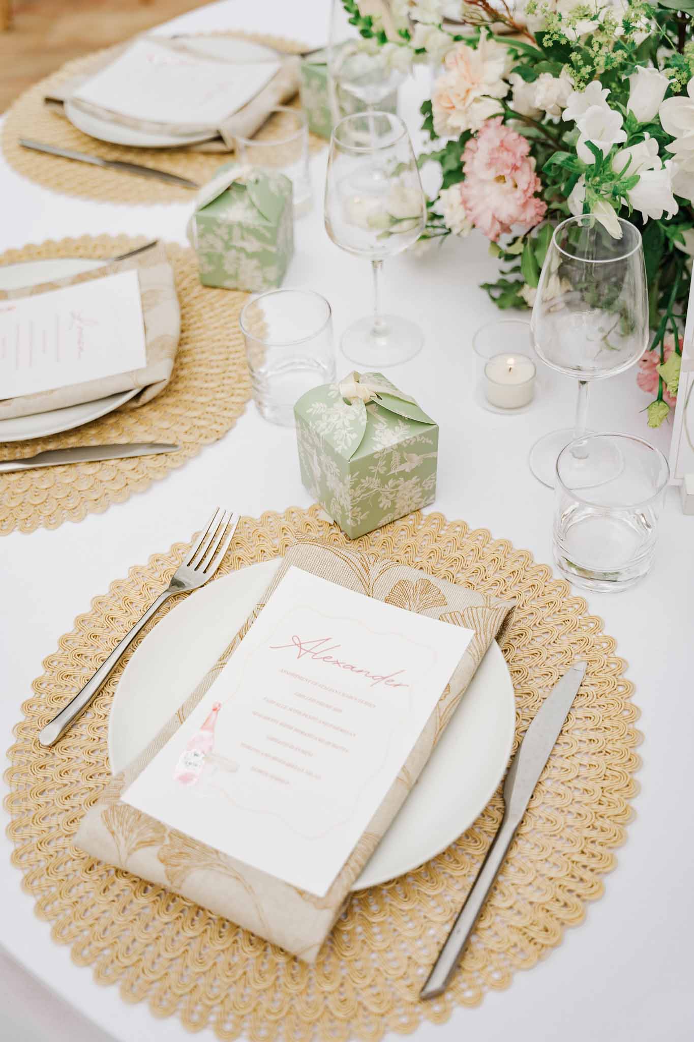 Elegant wedding table setting with white plates, sage green accents, and floral centerpiece at reception