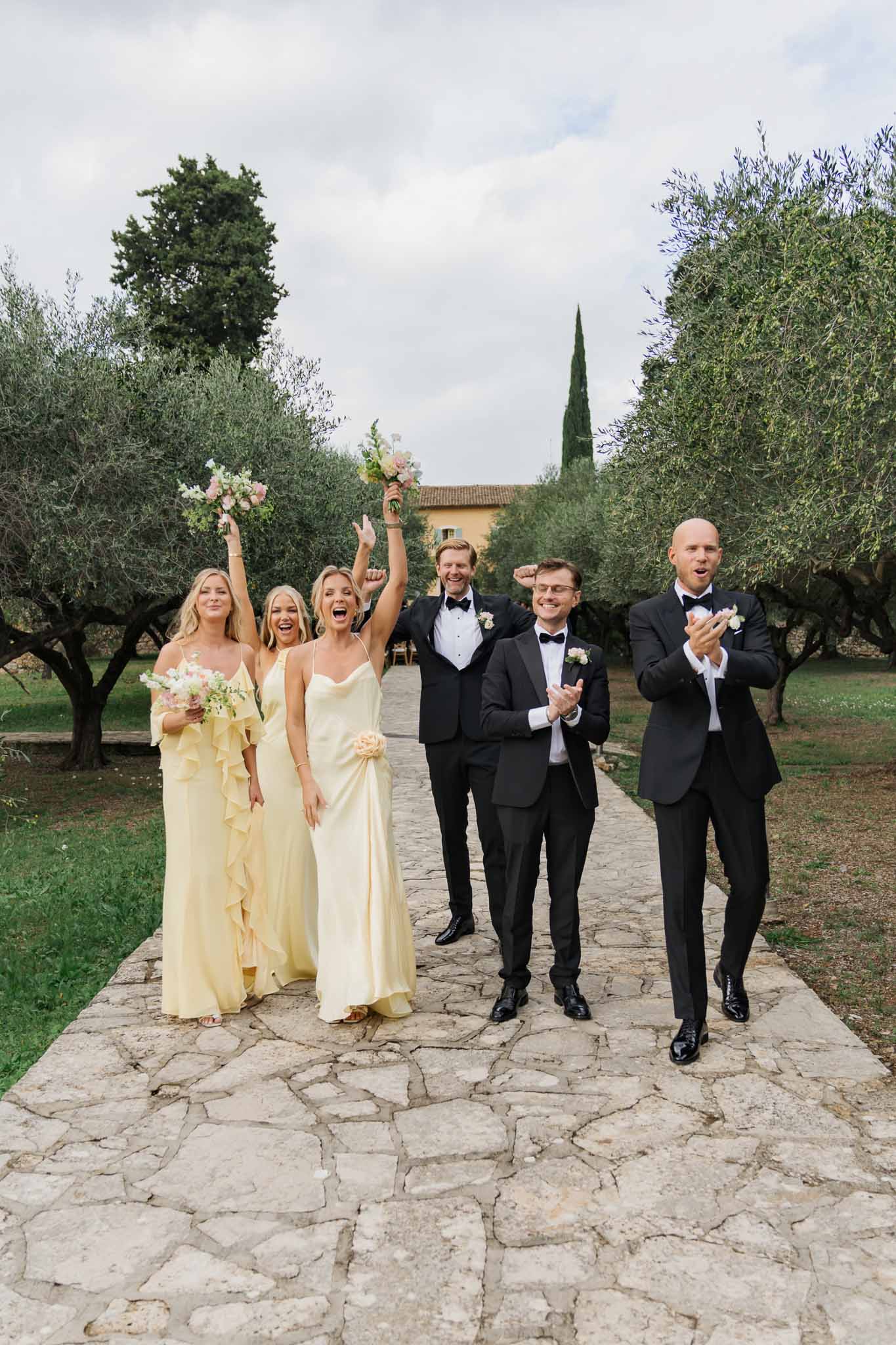 Bridal party celebrating on stone pathway in Tuscan olive grove with terracotta villa