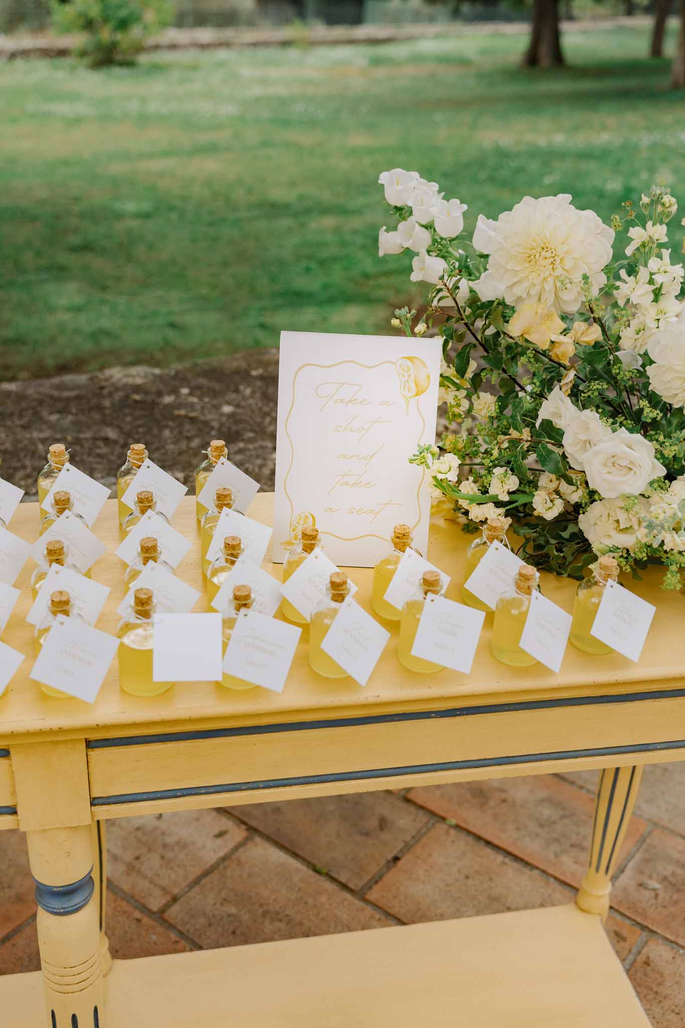 Wedding favor display with glass bottles and floral arrangement on outdoor terrace