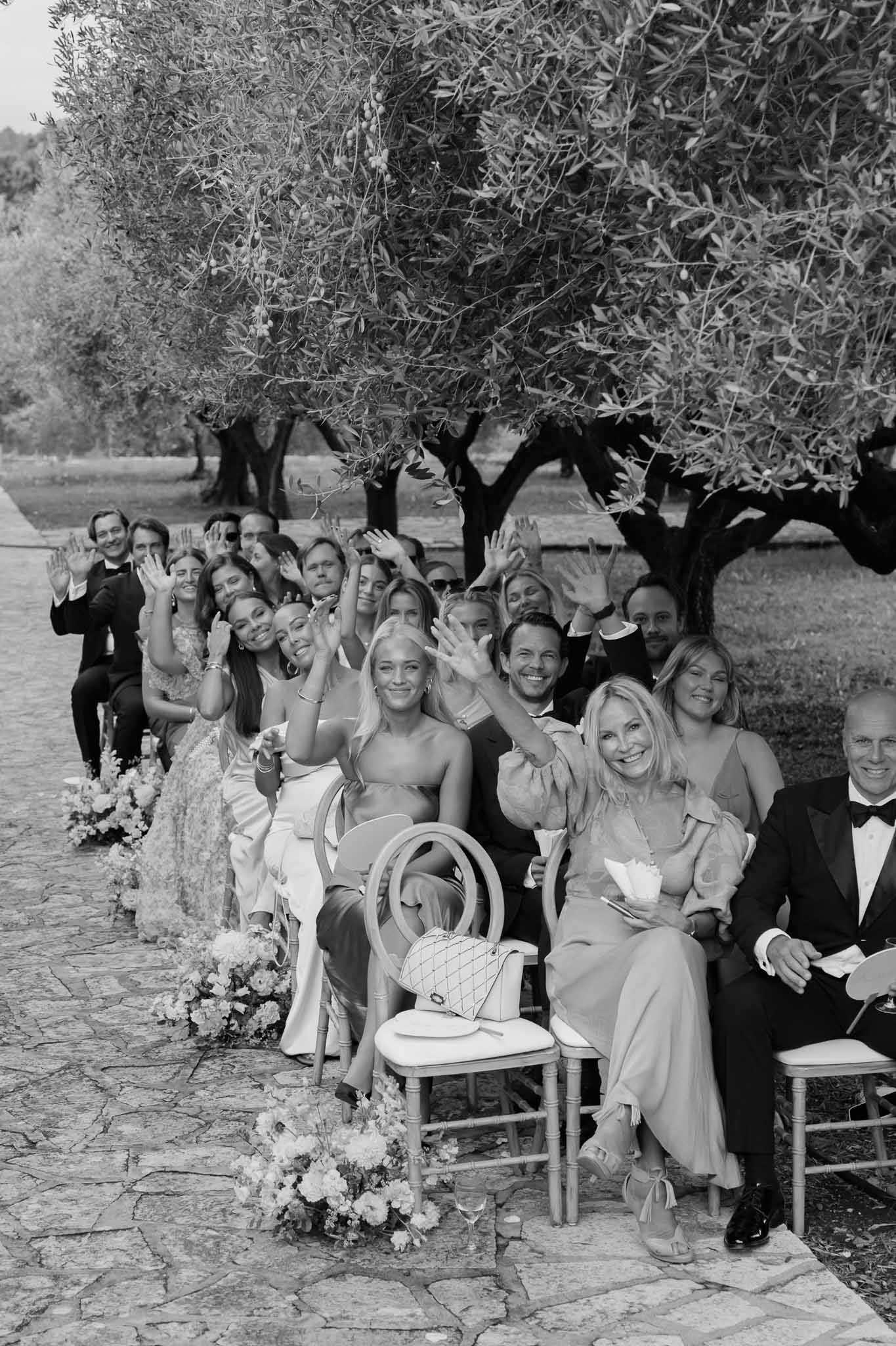 Outdoor wedding ceremony under olive trees with guests raising hands in celebration