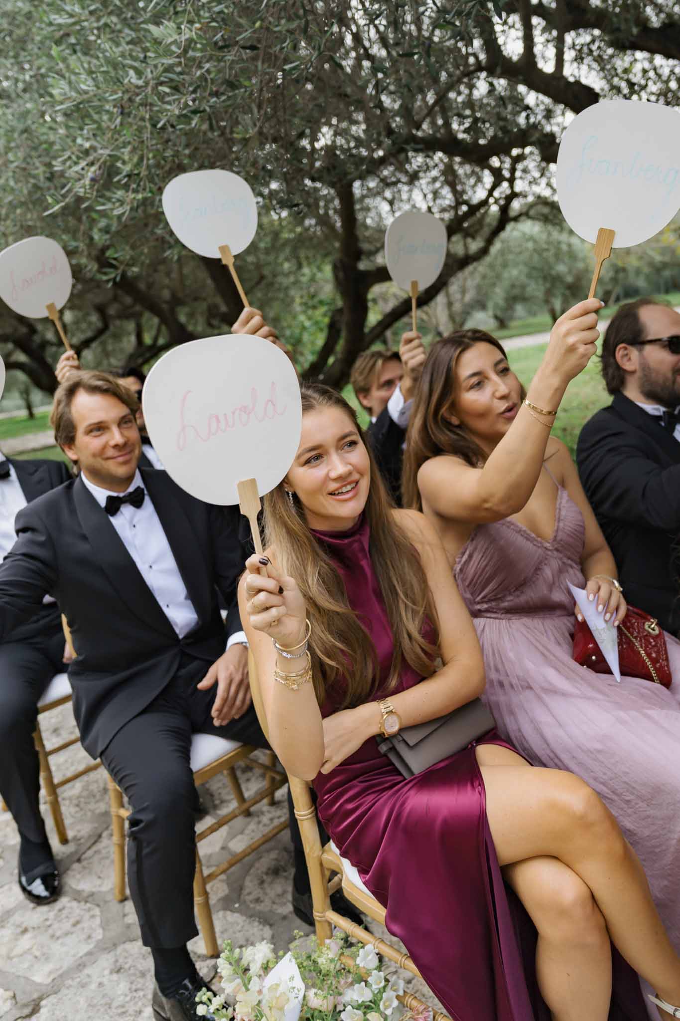 Wedding guests with ceremonial paddles during outdoor send-off in Mediterranean olive grove