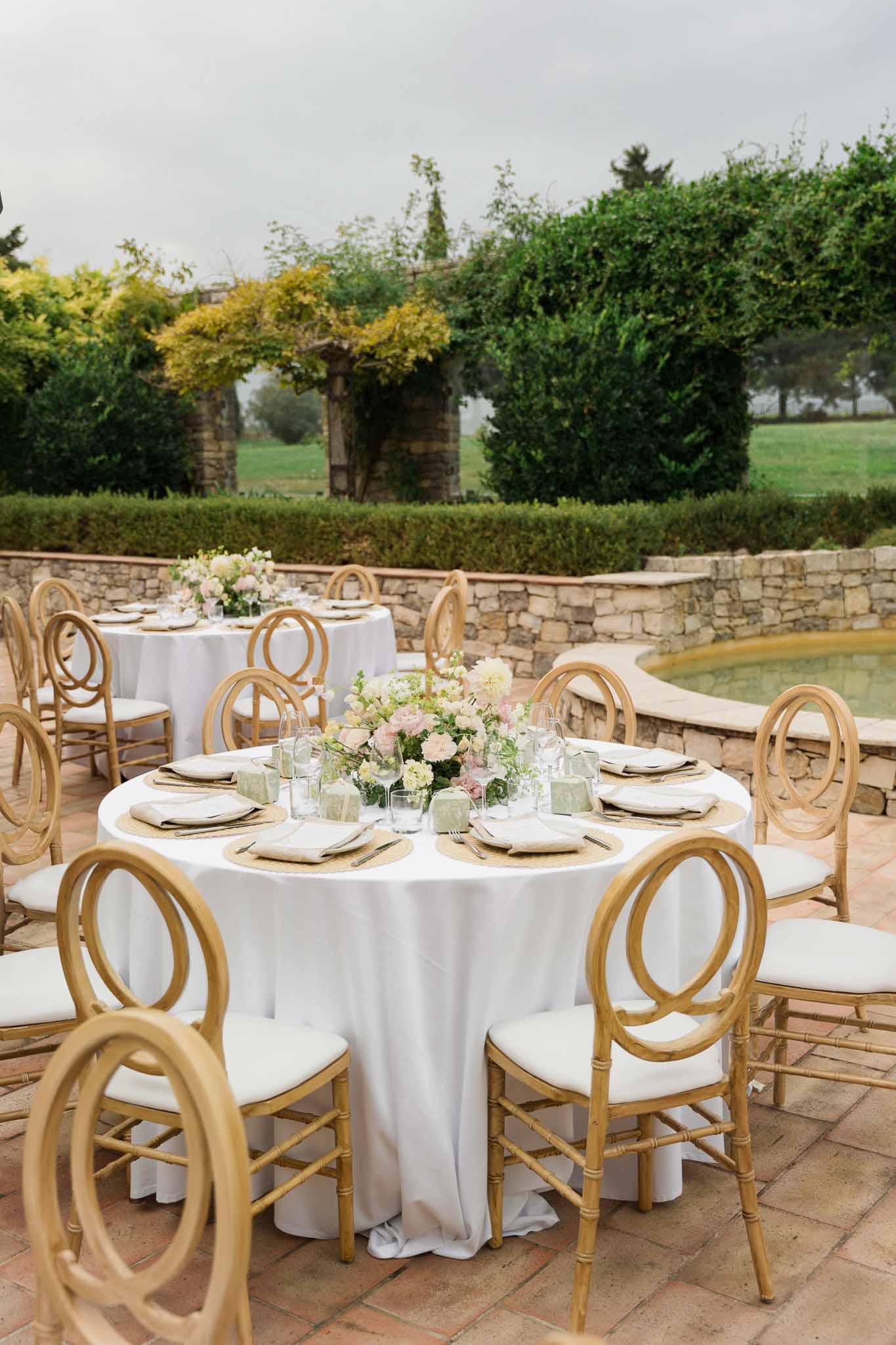 Reception tables with white linens and pink floral centerpieces on terracotta terrace overlooking formal gardens