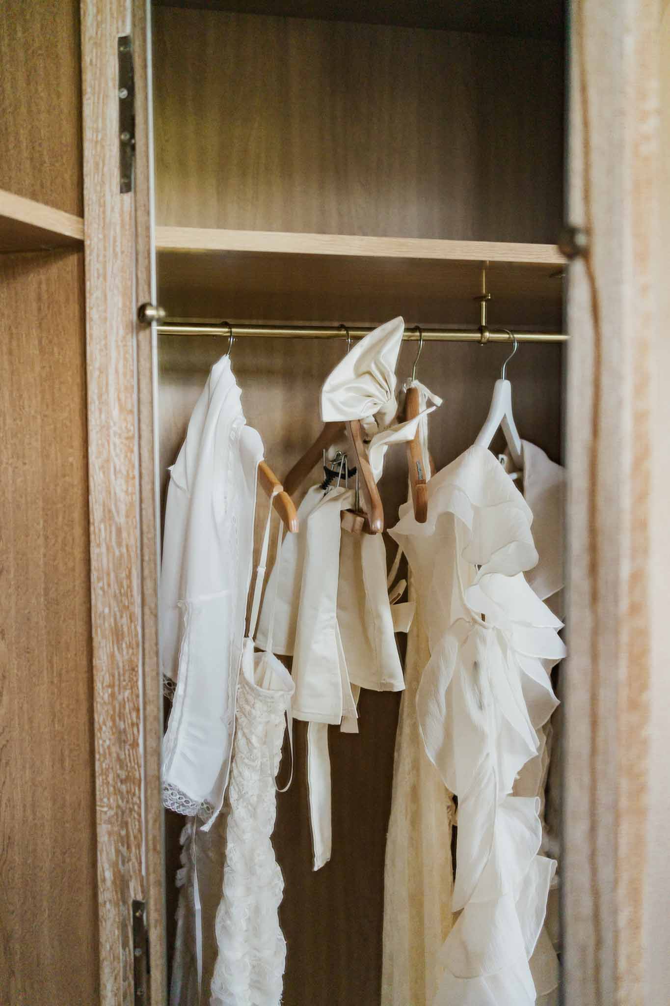 Bridal gown and bridesmaid dresses hanging in wooden wardrobe during wedding preparation