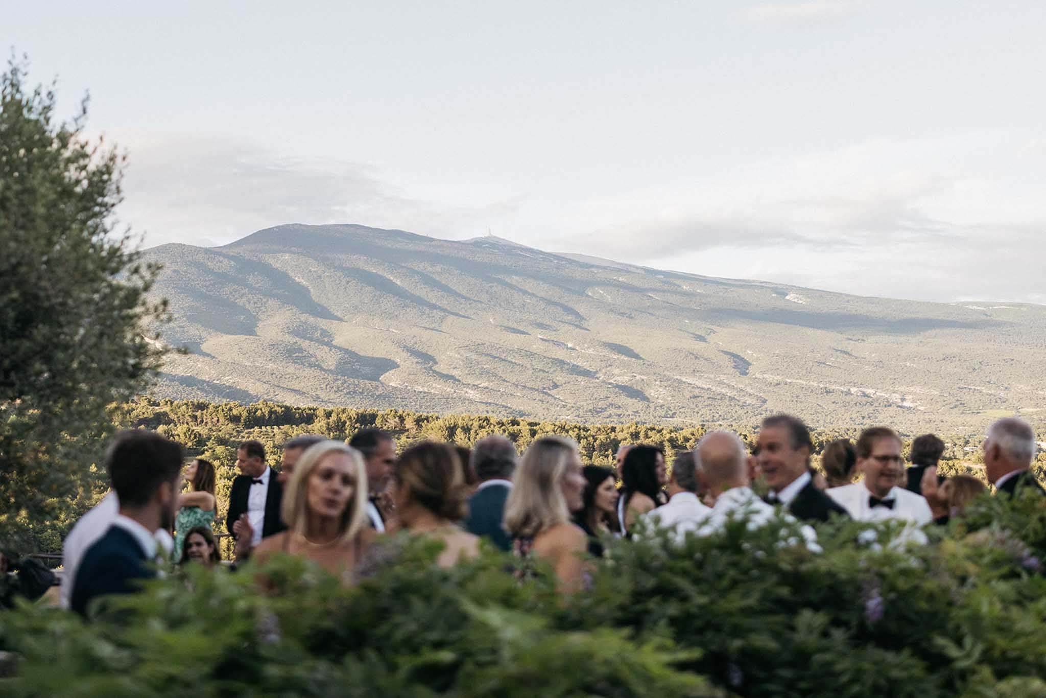 Wedding guests mingling during cocktail hour at outdoor hilltop venue with mountain views