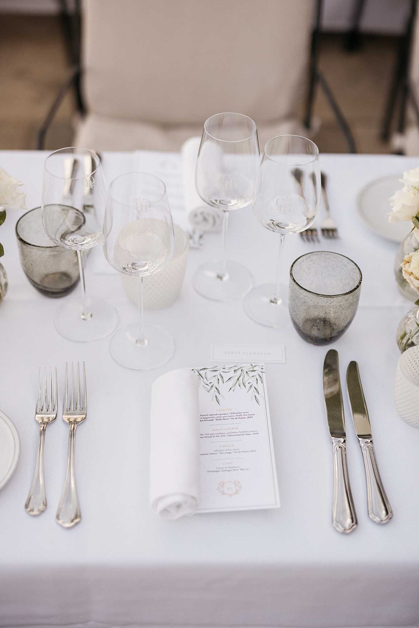 Elegant white reception table setting with silver flatware and botanical menu cards at wedding venue