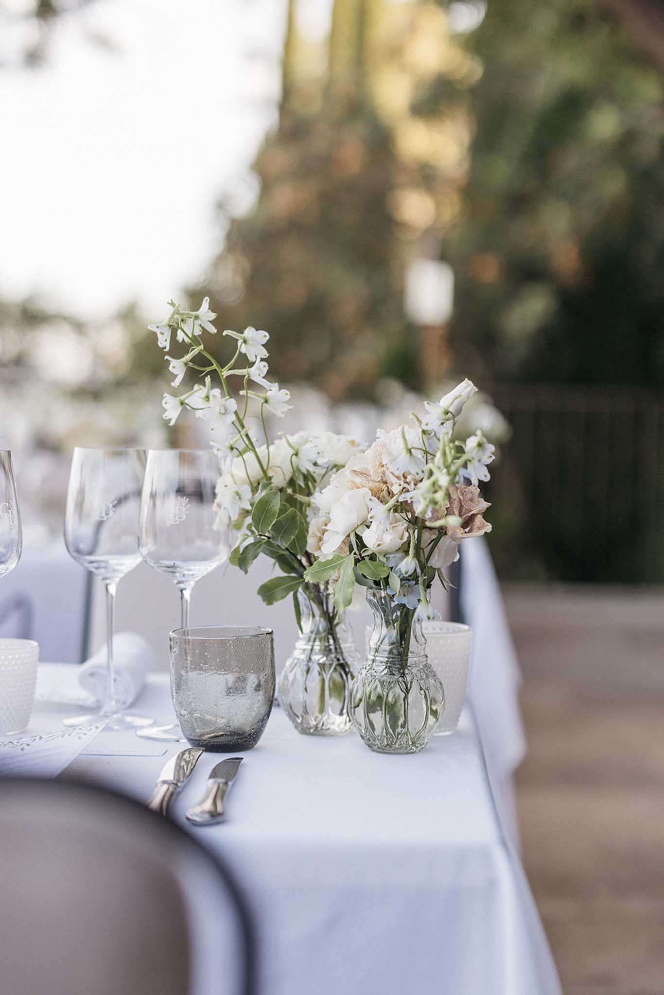 Wedding reception table setting with white florals and glass centerpieces at Mediterranean garden venue