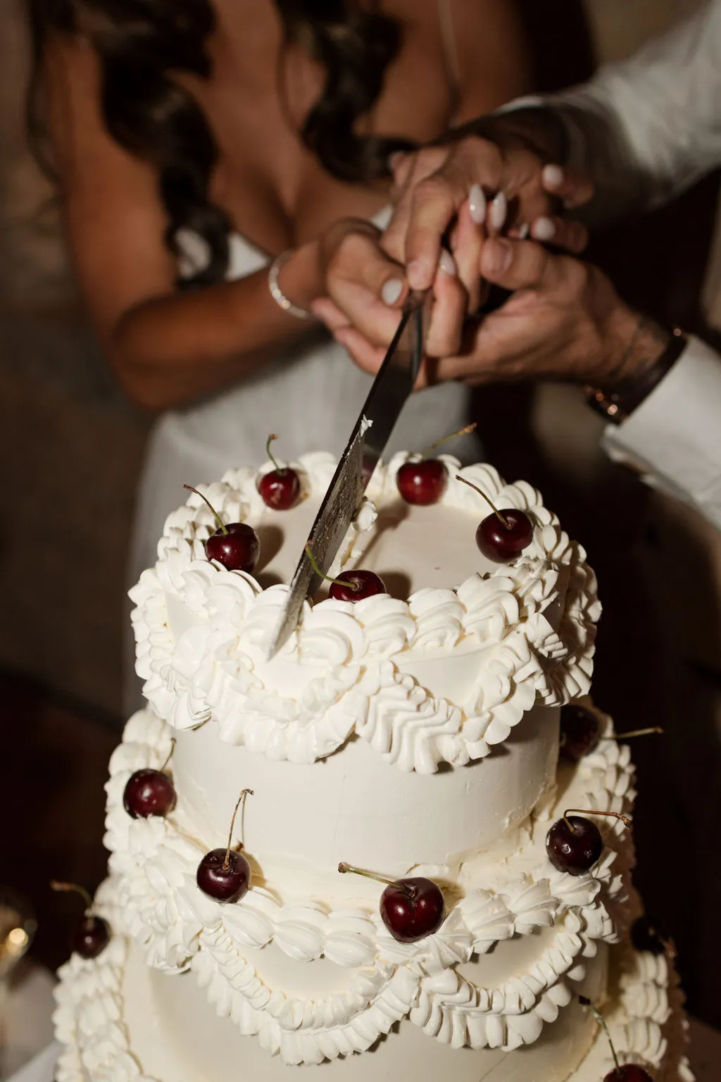 Bride and groom cutting white buttercream wedding cake decorated with red cherries during reception ceremony
