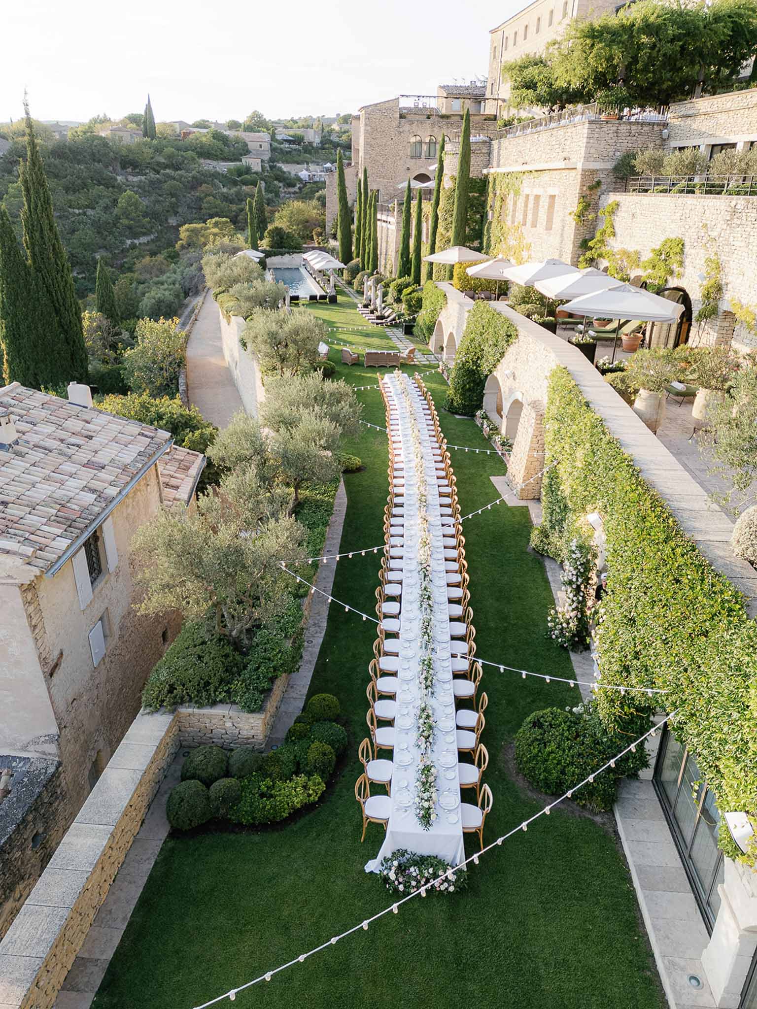 Aerial view of wedding reception setup in historic stone courtyard with long banquet table and cypress trees