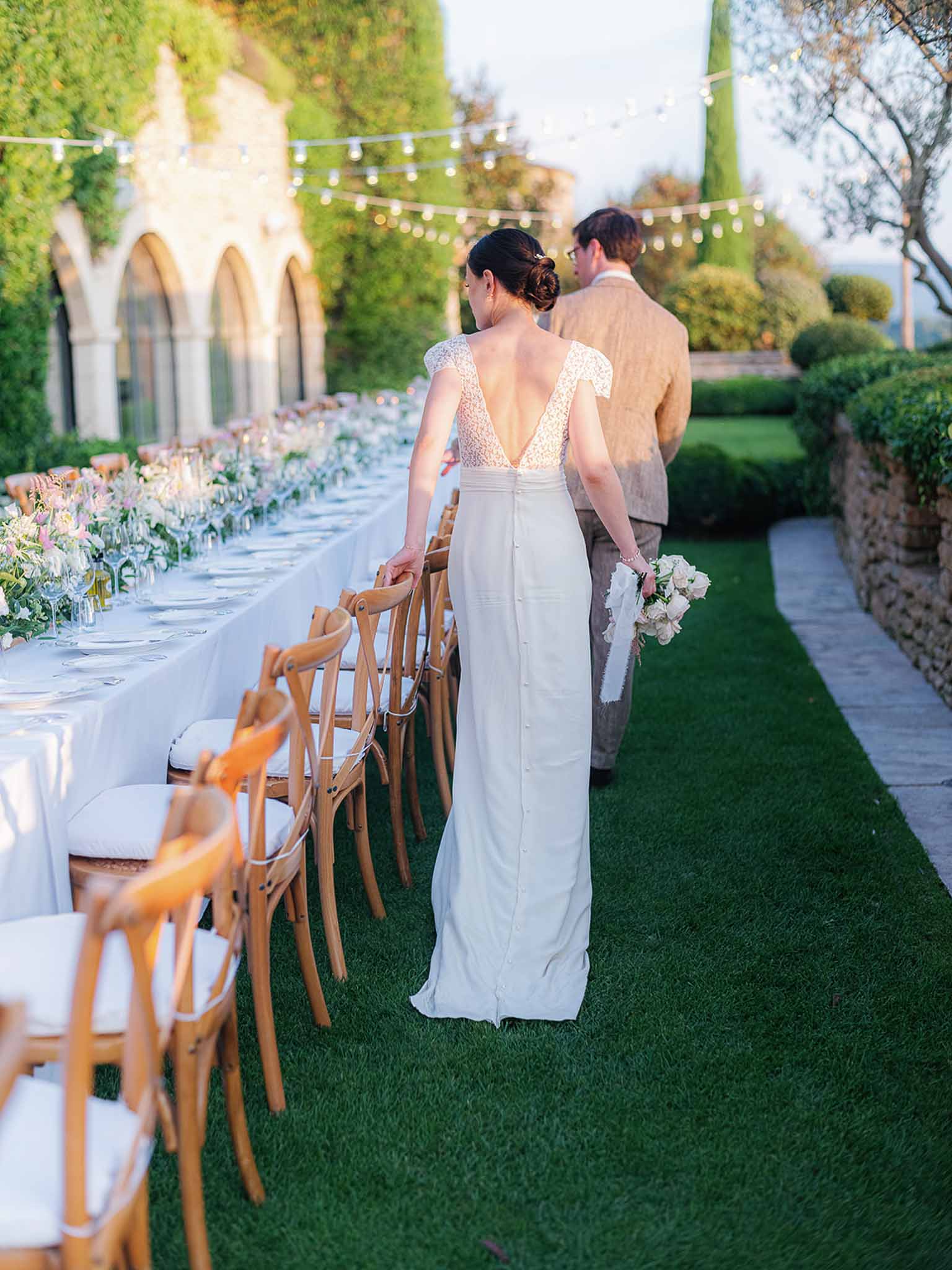 Bride and groom walking down ceremony aisle in garden courtyard with ivy-covered stone architecture