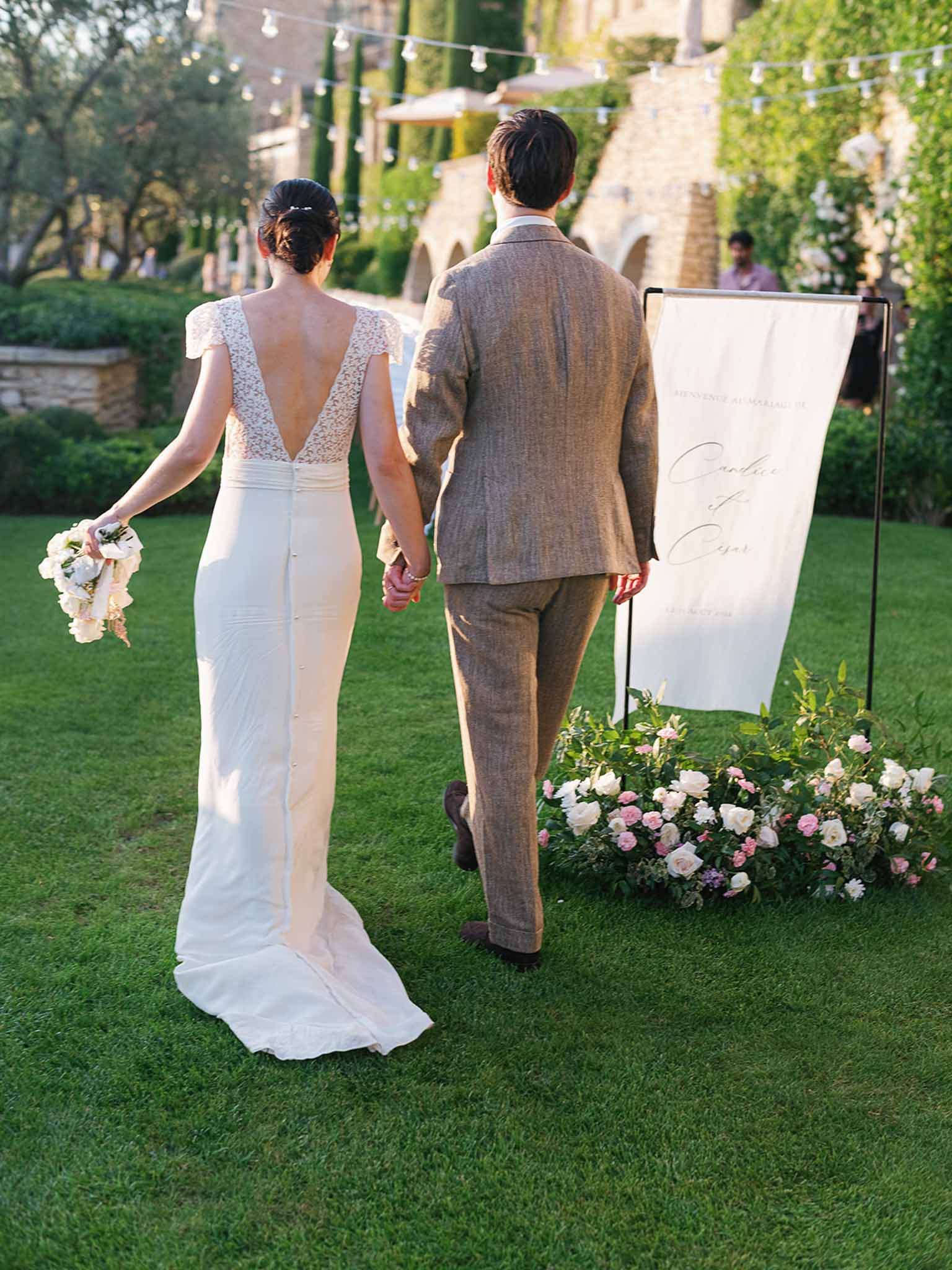 Bride and groom walking hand-in-hand during outdoor ceremony in walled garden with ivy-covered stone buildings