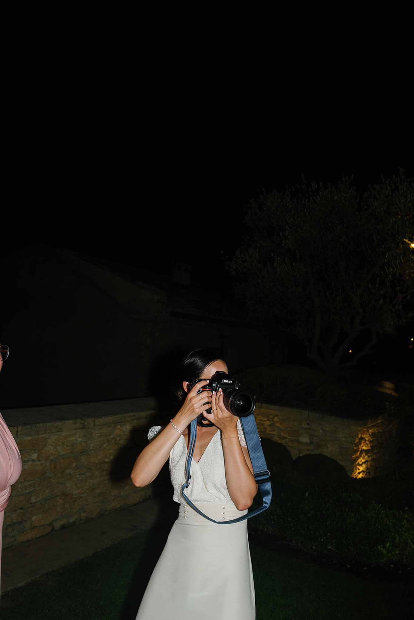 Wedding photographer in white dress capturing reception moments at outdoor stone terrace venue