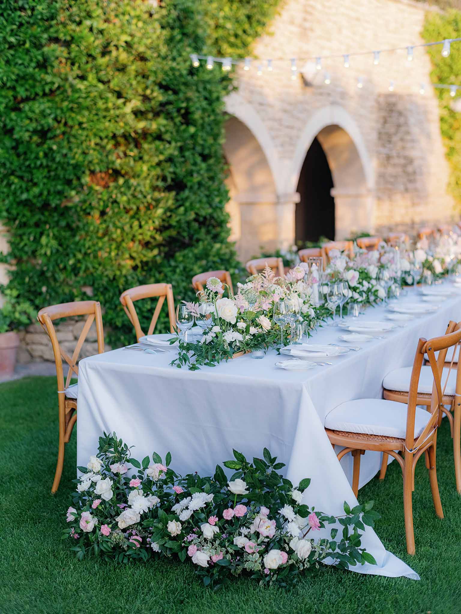 Outdoor reception table with white and pink florals in courtyard with stone architecture