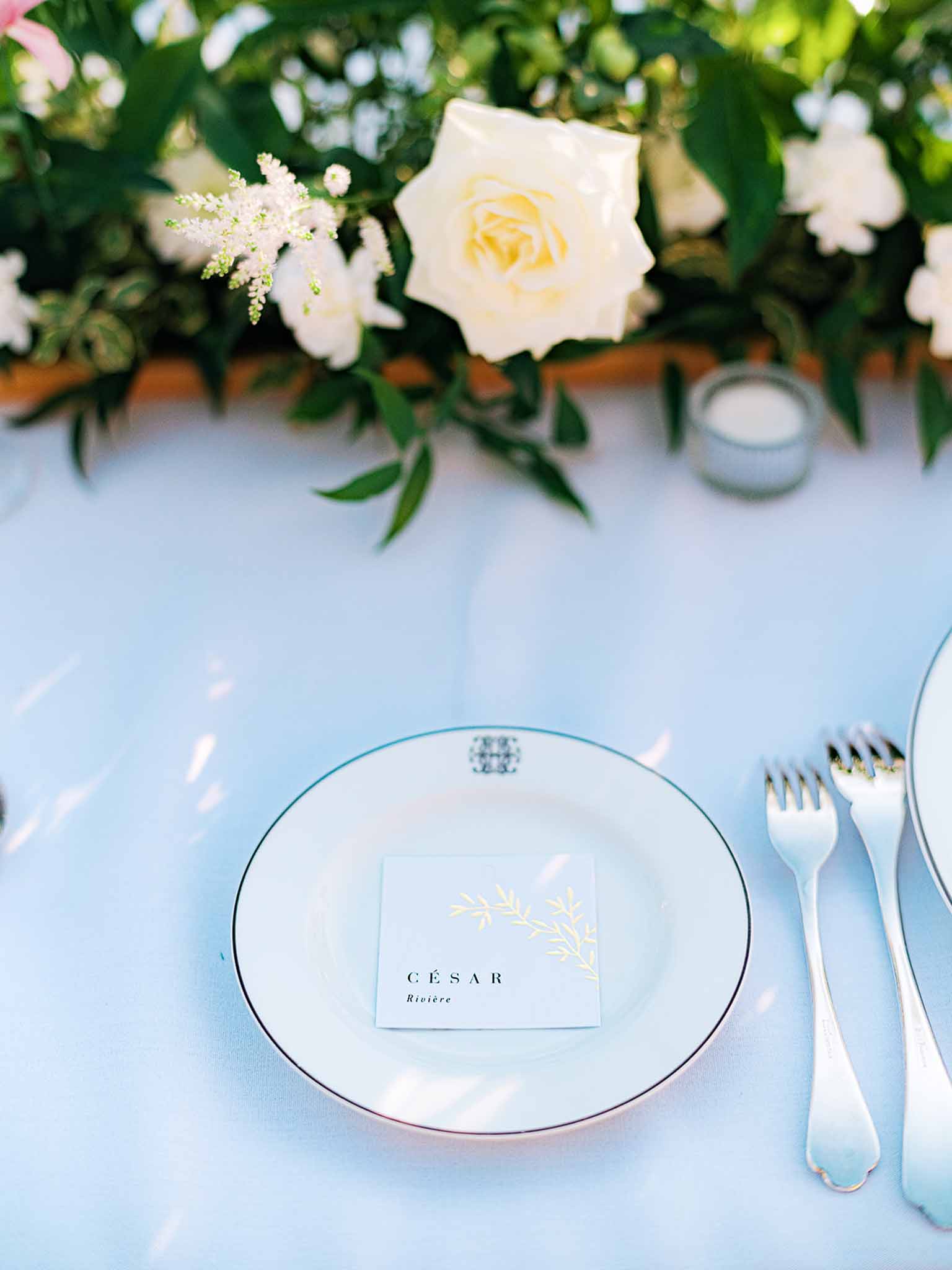Elegant table setting with pale blue linen, floral centerpiece, and place card at wedding reception