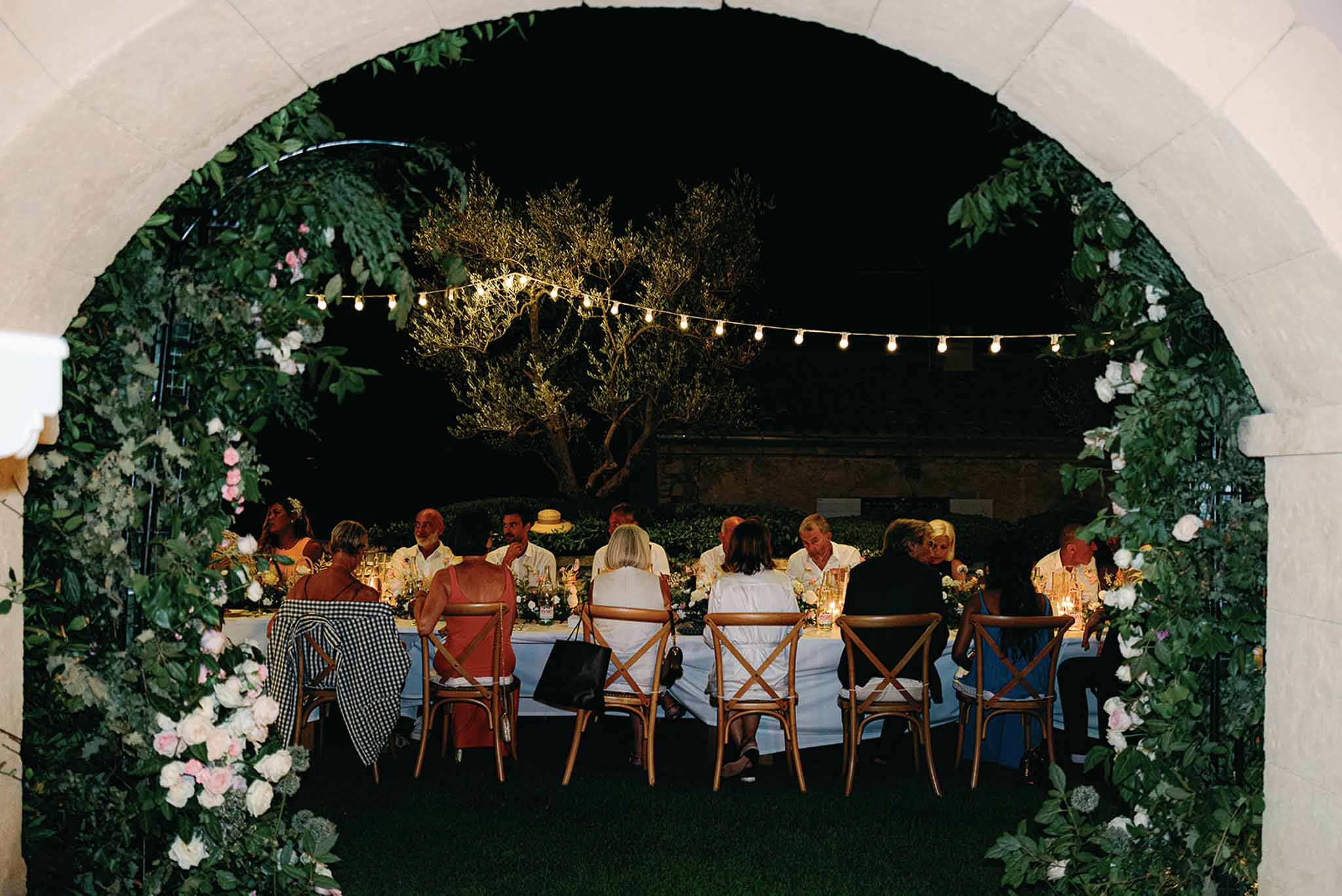 Nighttime wedding reception dinner under marquee tent with string lights and floral entrance