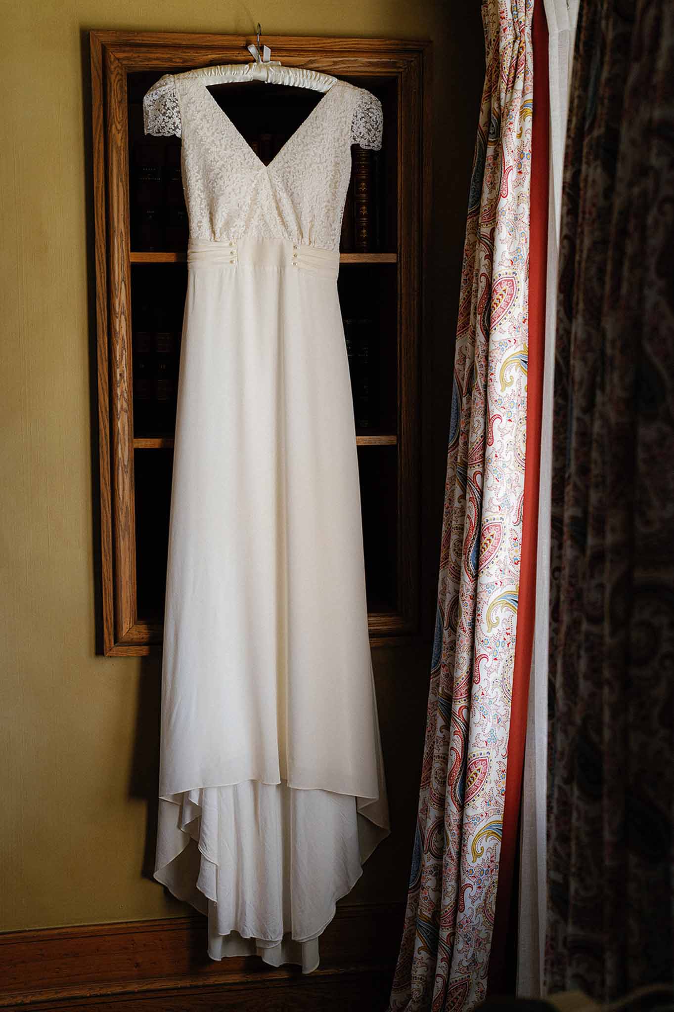 Ivory bridal gown with lace cap sleeves hanging in getting-ready space