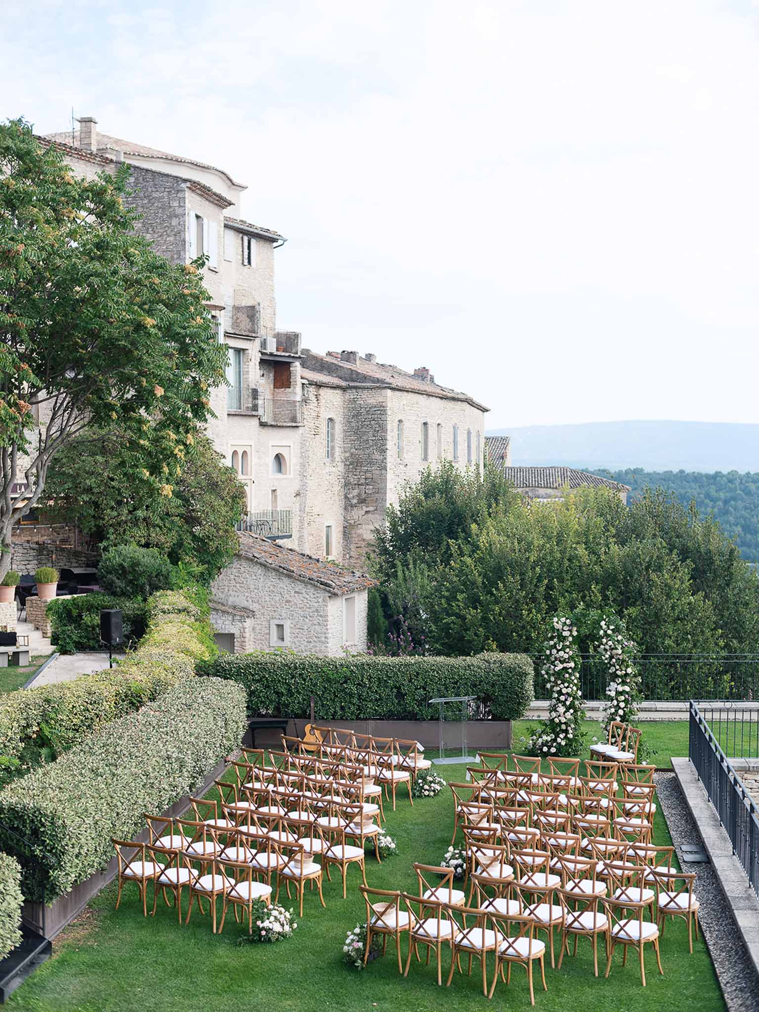 Wedding ceremony setup on terrace overlooking Italian hilltop village with stone manor house backdrop