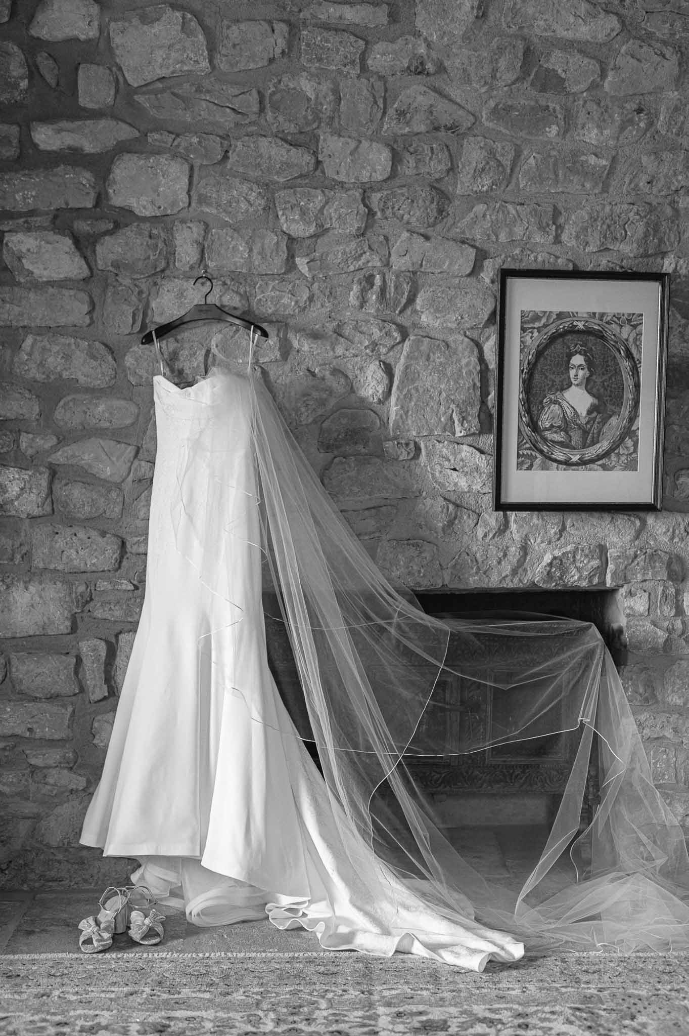 Bride's wedding dress and veil hanging on wooden hanger against stone wall during getting ready preparations
