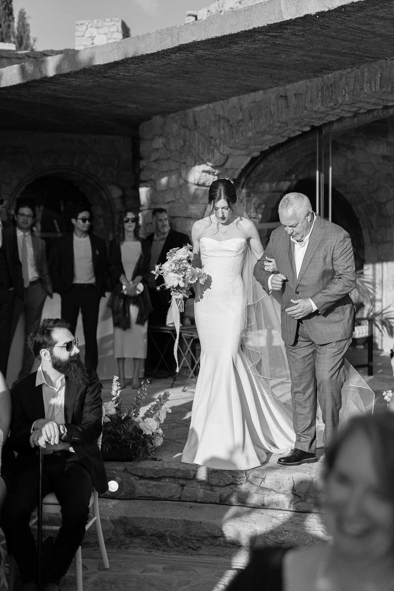 Wedding ceremony processional through stone archway at historic outdoor venue