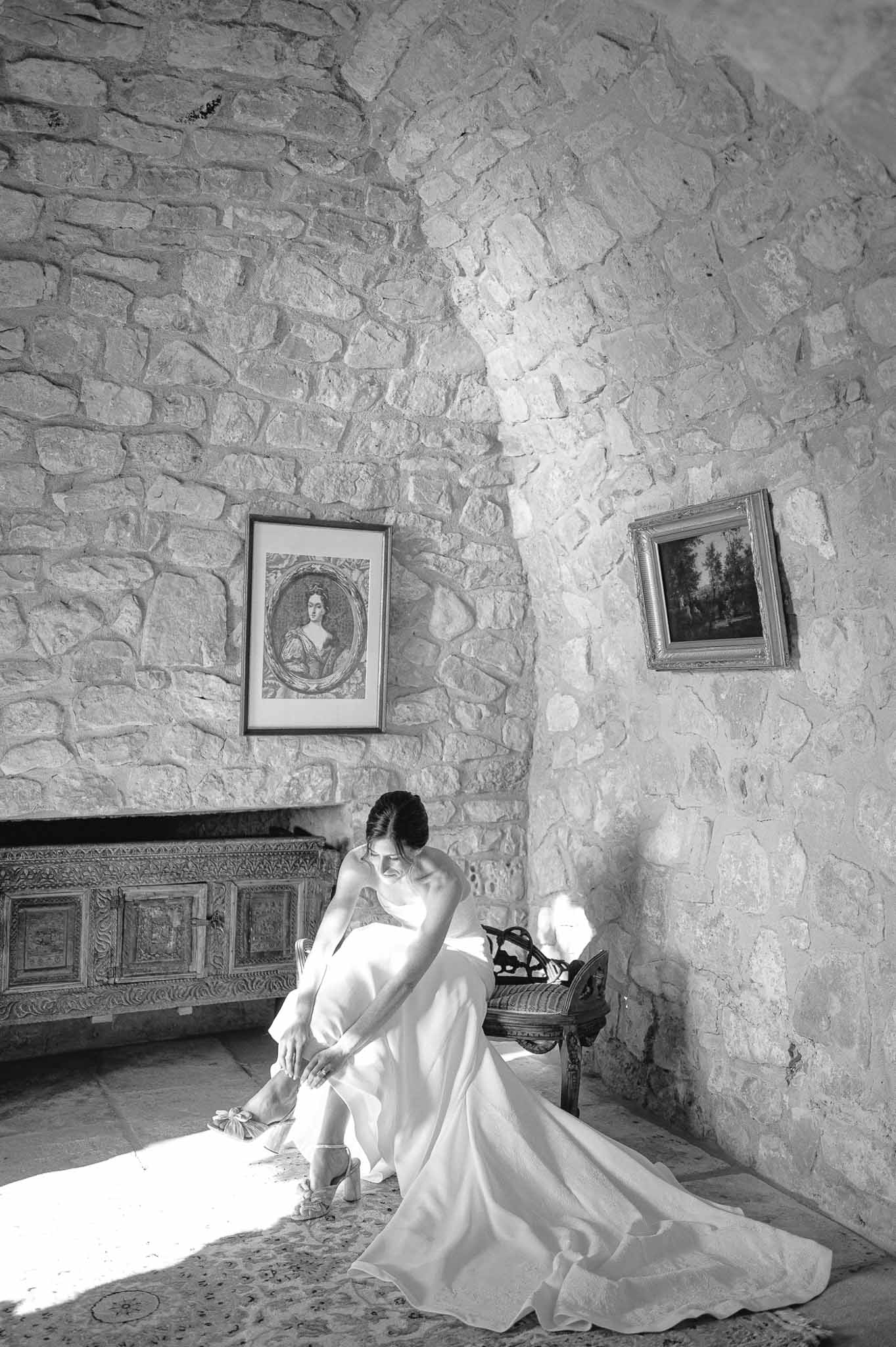 Bride in white wedding dress sitting in historic stone chamber with fireplace and artwork