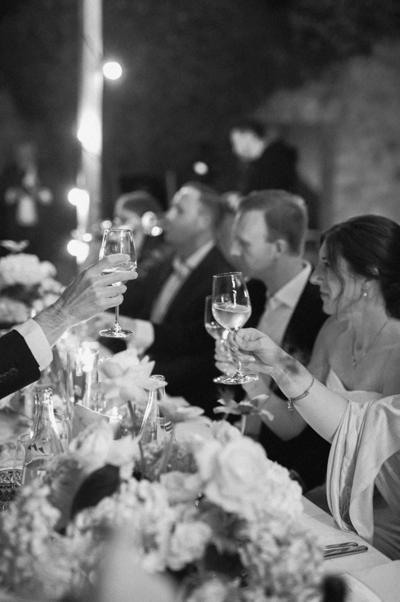 Wedding guests raising wine glasses in toast at outdoor reception dinner table with floral centerpieces