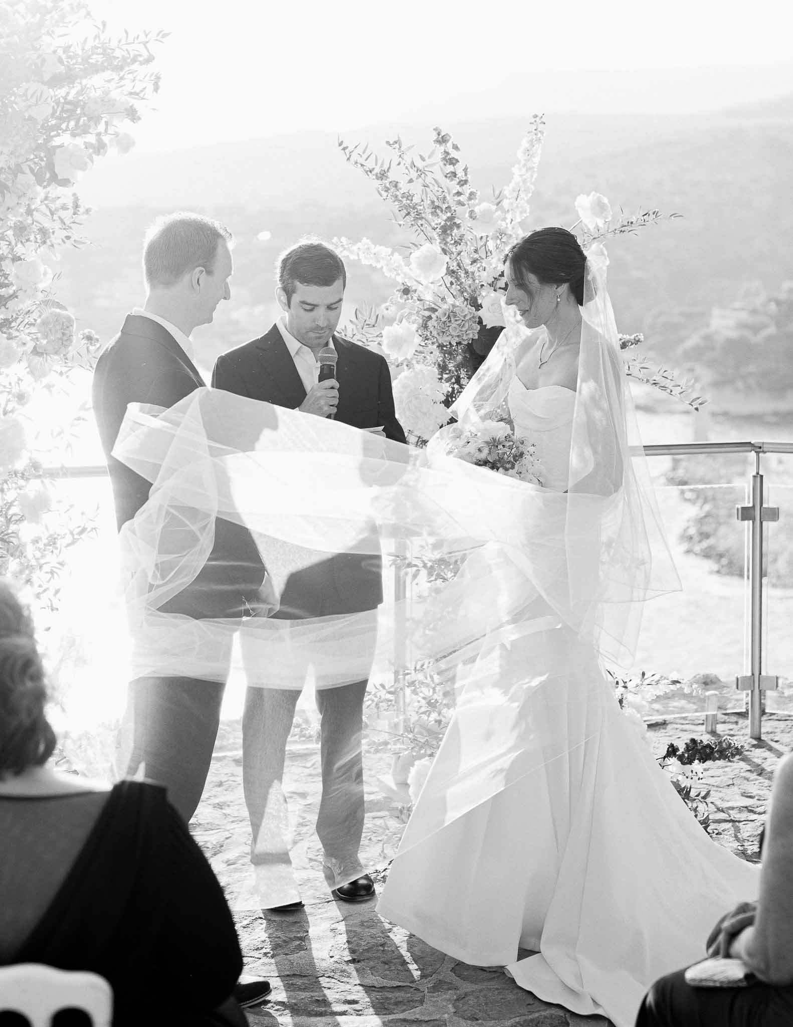 Bride and groom exchanging vows with officiant at outdoor hillside wedding ceremony
