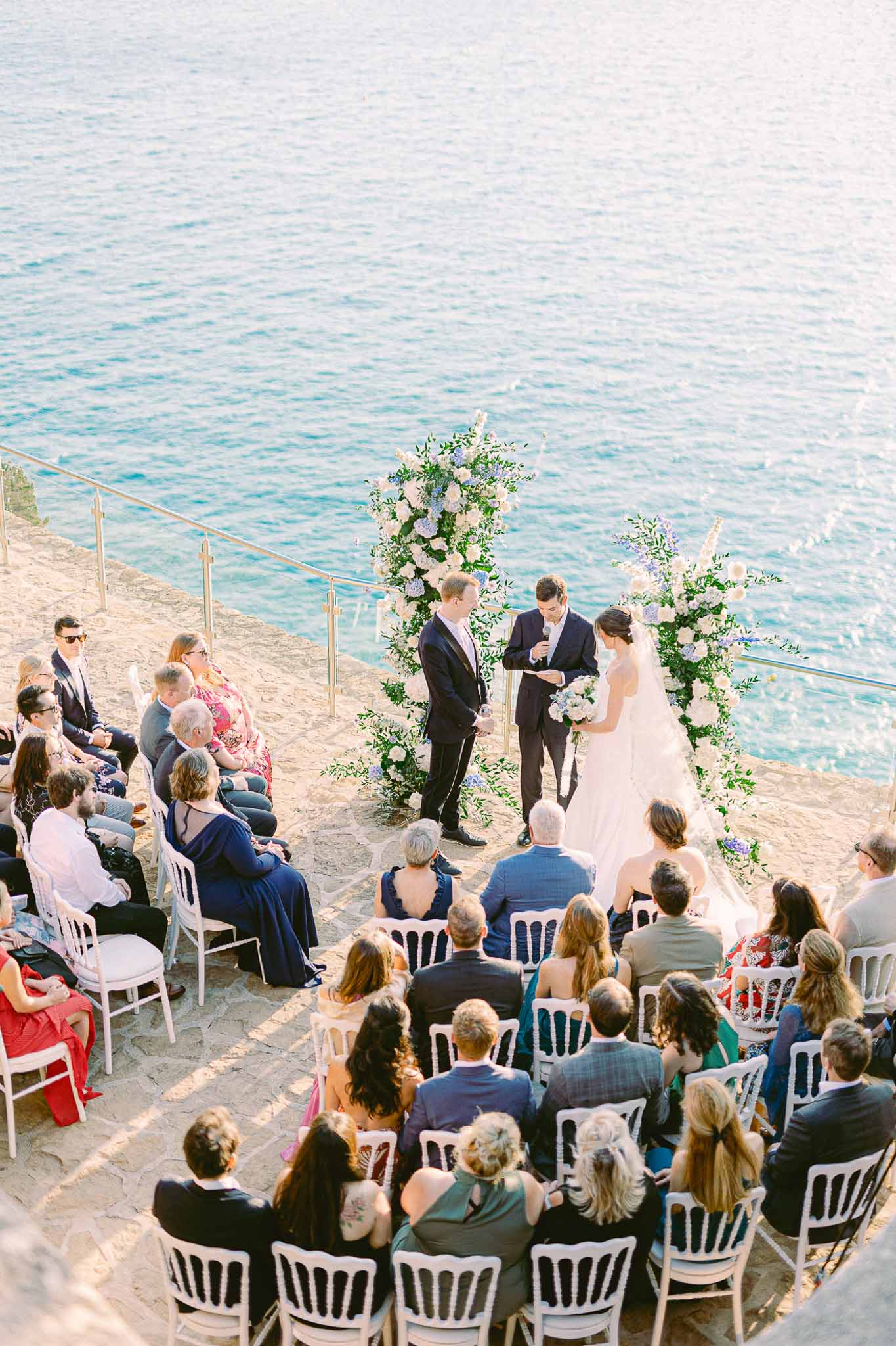 Beachside wedding ceremony with floral arch and seated guests overlooking turquoise water