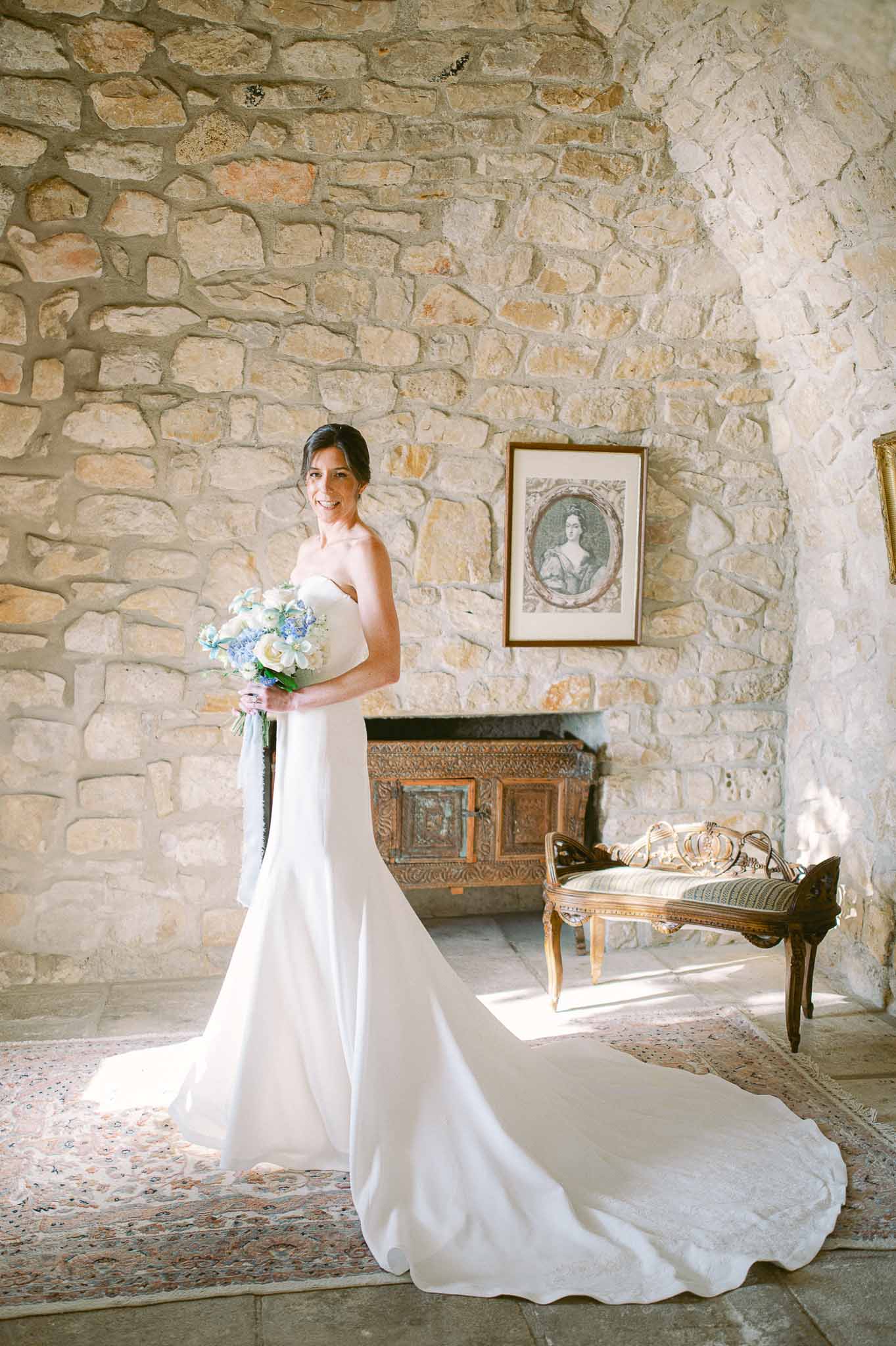 Bride in ivory dress holding blue hydrangea bouquet in stone-walled interior room